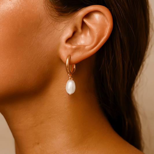 Close-up of an ear wearing a gold hoop earring with a pearl pendant.