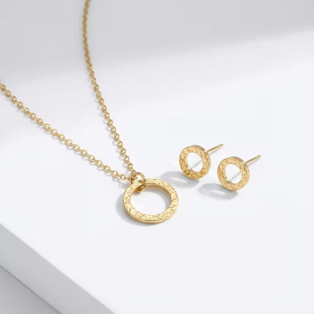 Gold circle necklace and matching studs on a light gray background