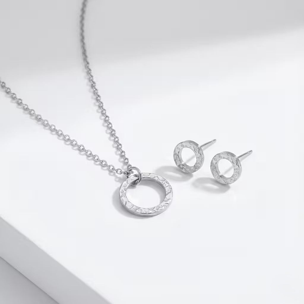 Silver circle necklace and matching studs on a light gray background