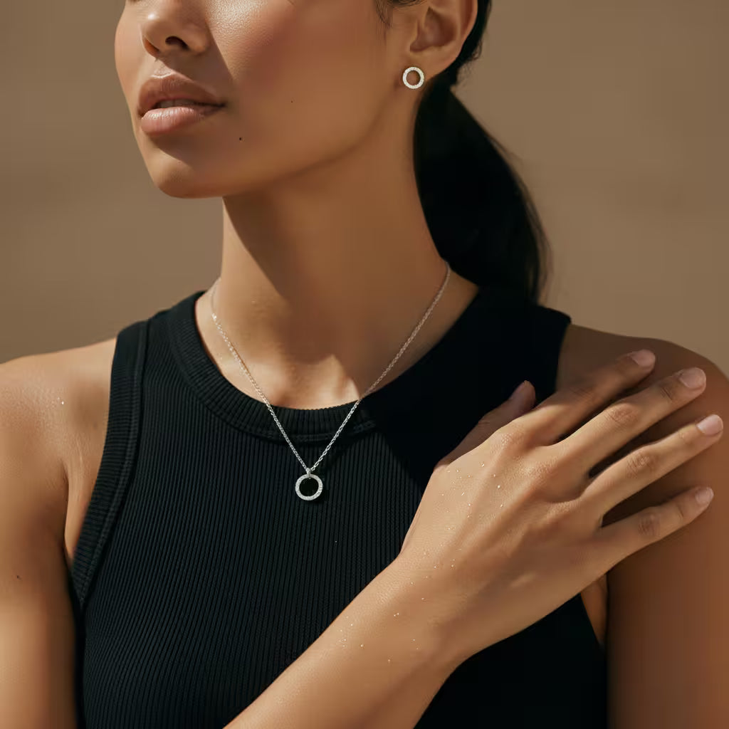 Woman wearing a silver circle necklace and matching stud earrings against a warm brown background