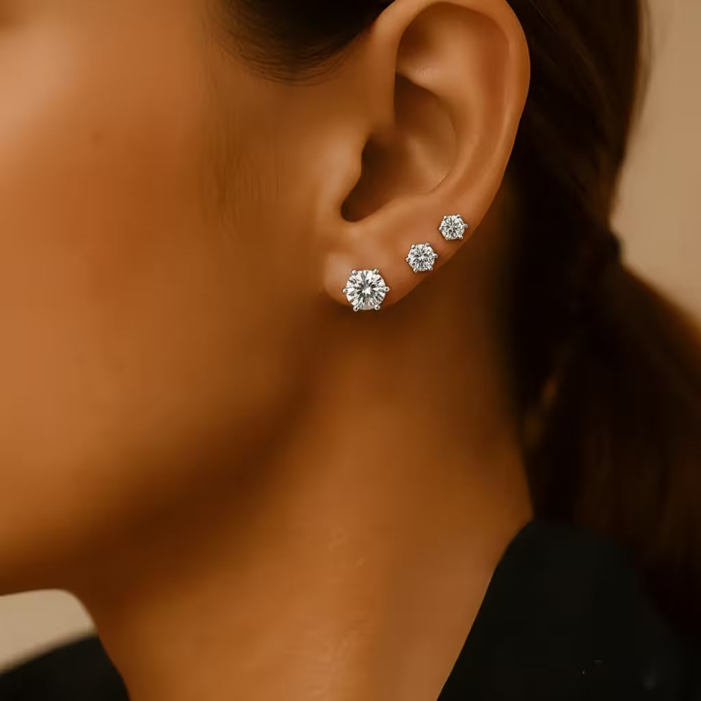 Close-up of a person wearing three diamond stud earrings on a blurred background