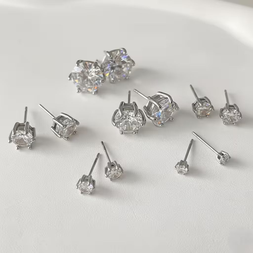 Different sizes of silver stud earrings on a light gray background