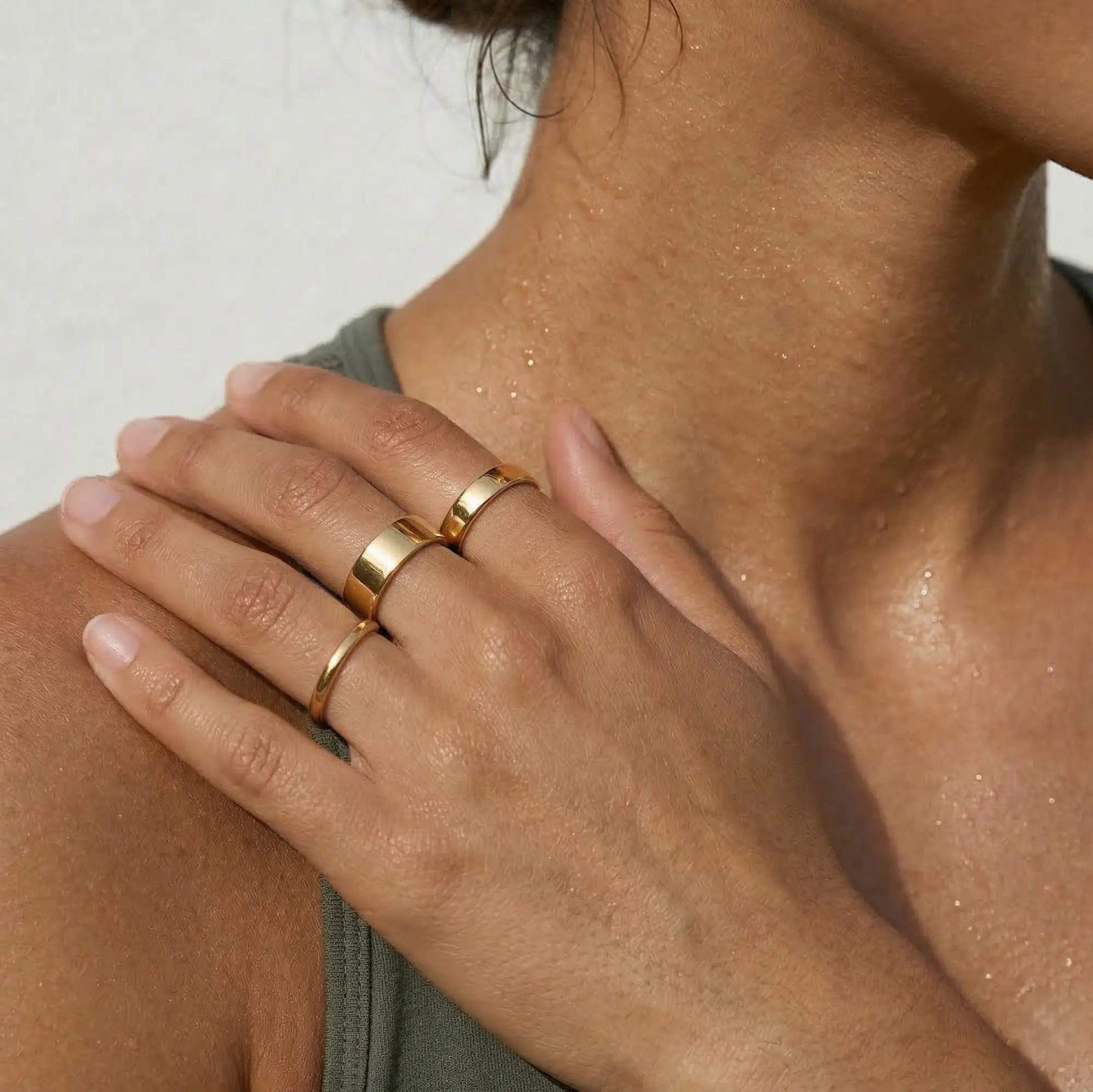 Close-up of a woman wearing three gold rings on a neutral background.
