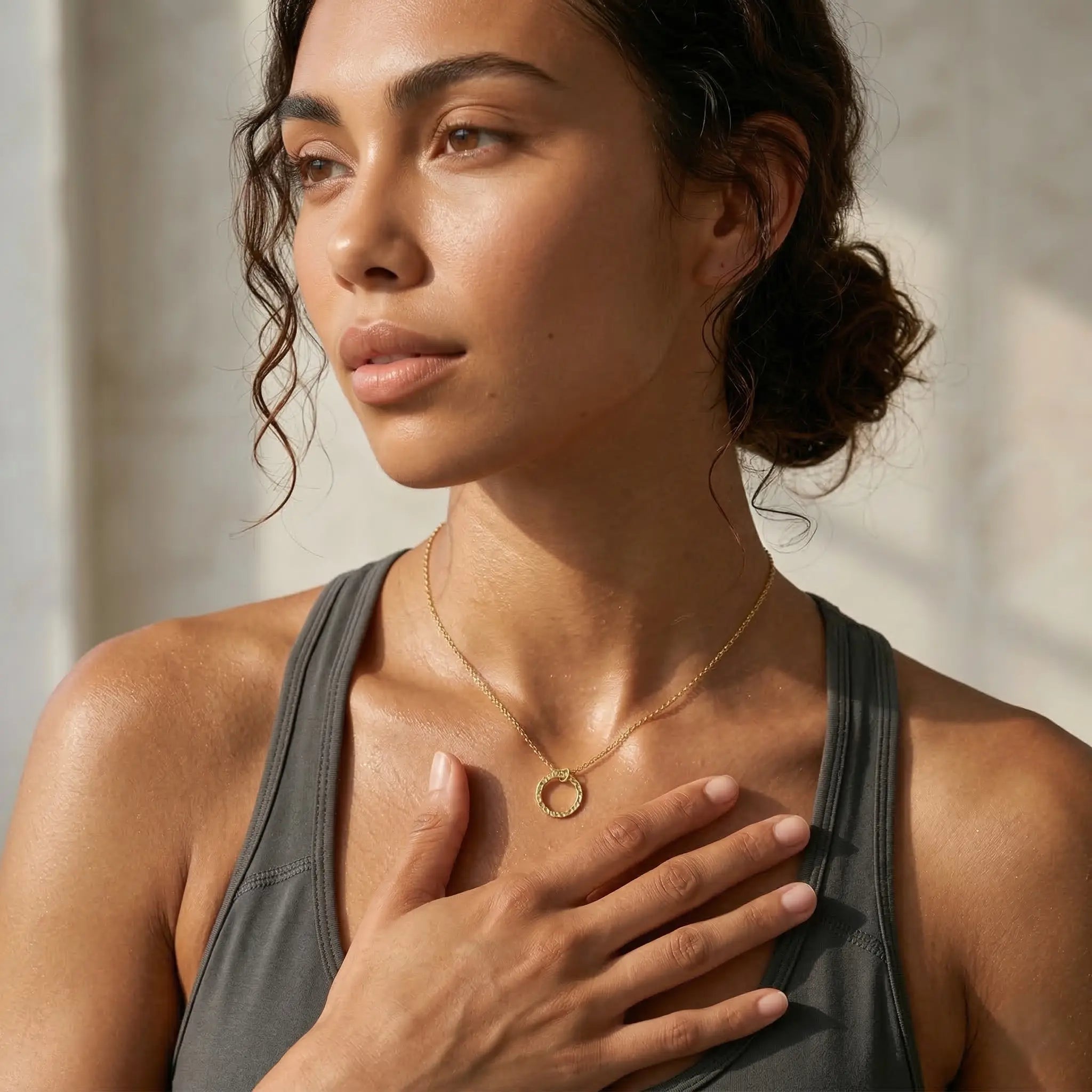 Woman wearing a gold necklace with a circular pendant, against a neutral background.