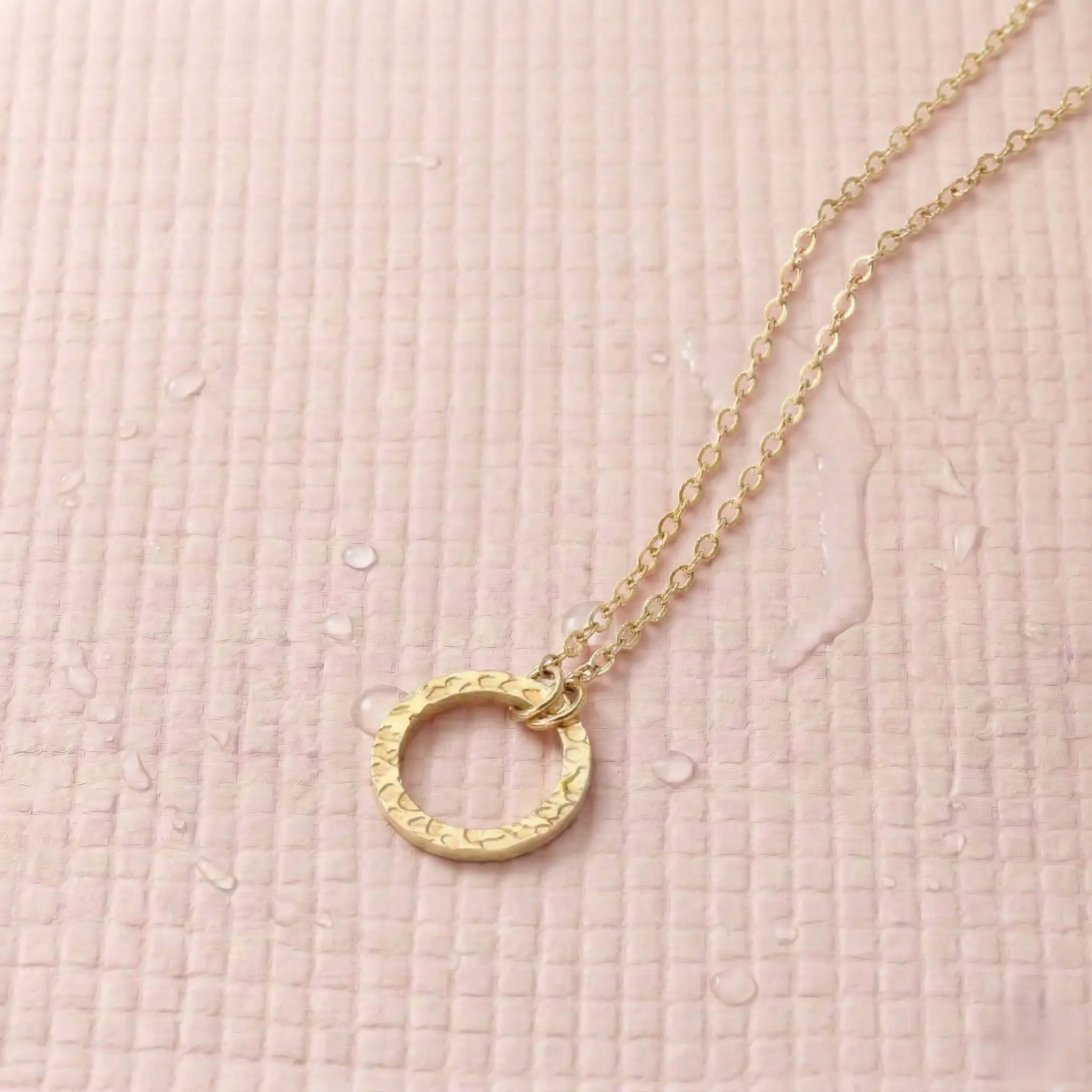  Gold-plated necklace with a circle pendant on a light pink fitness mat.