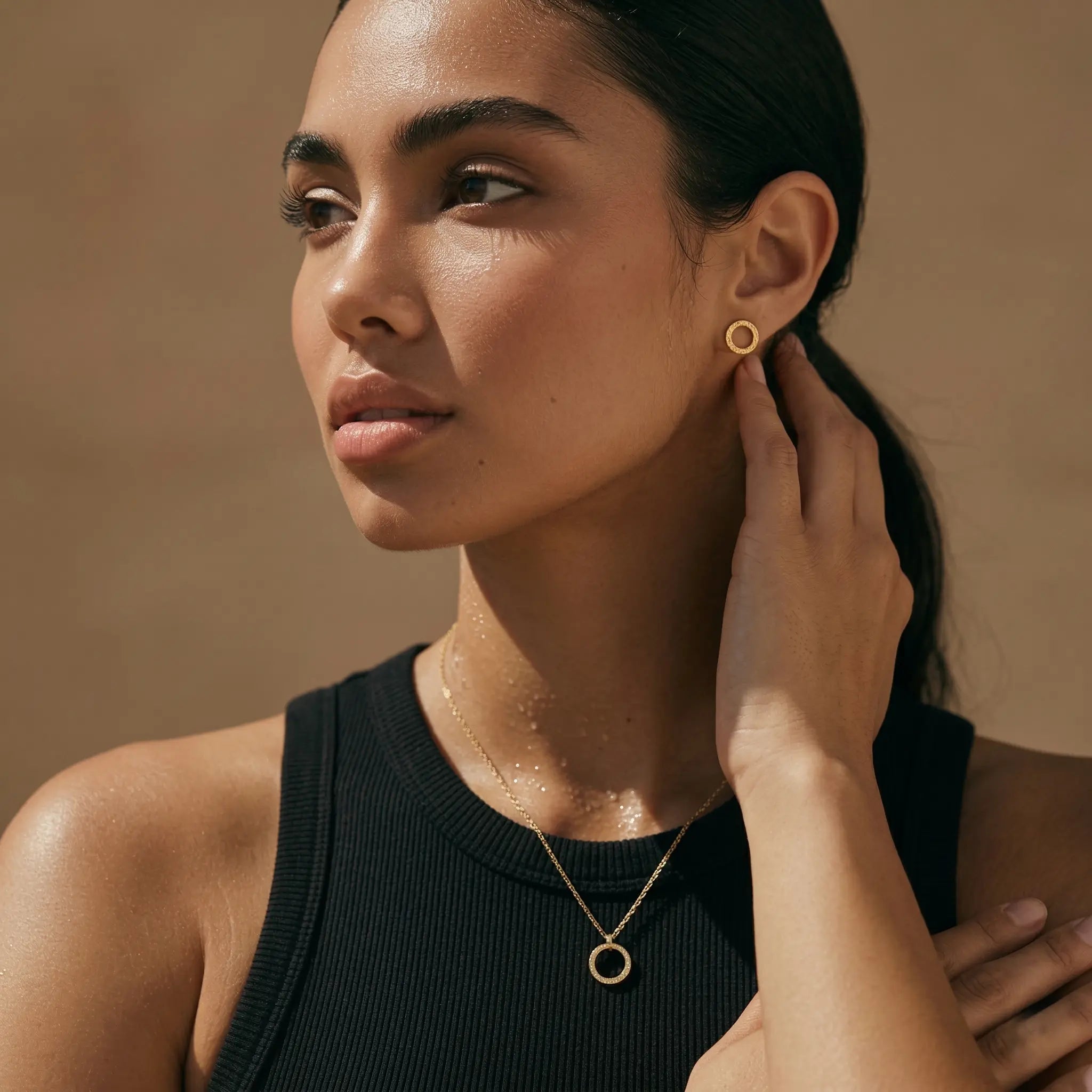 Woman wearing gold circle necklace and matching studs against a beige background.