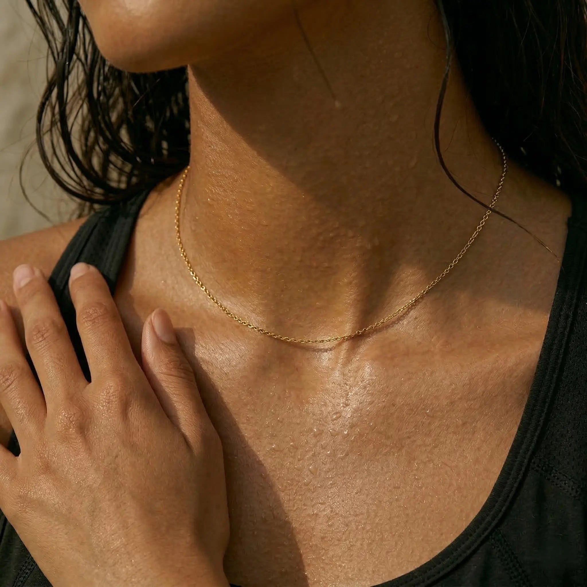 Close-up of a woman wearing a gold necklace with water droplets on skin.