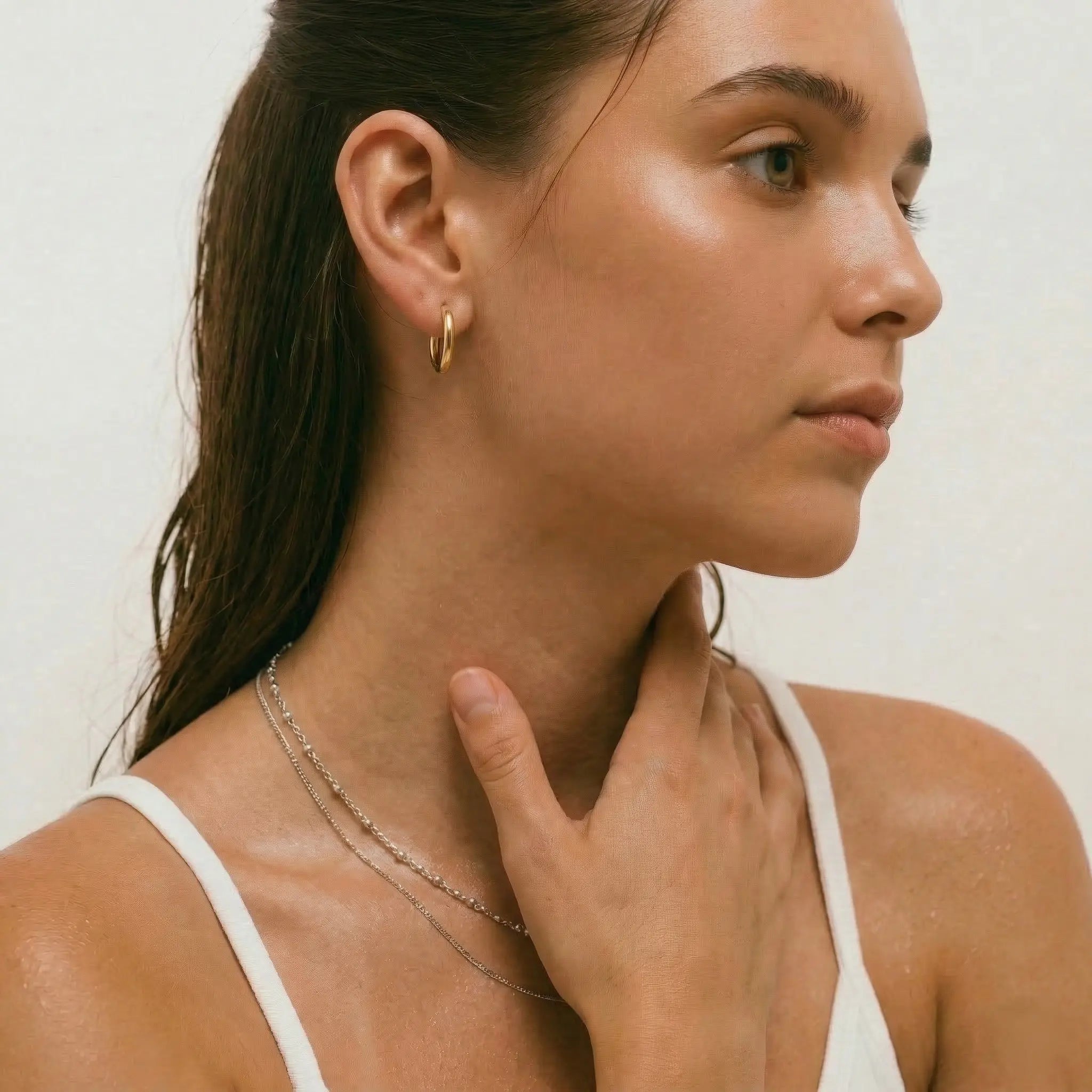 Woman wearing a gold hoop earring and necklace against a neutral background.