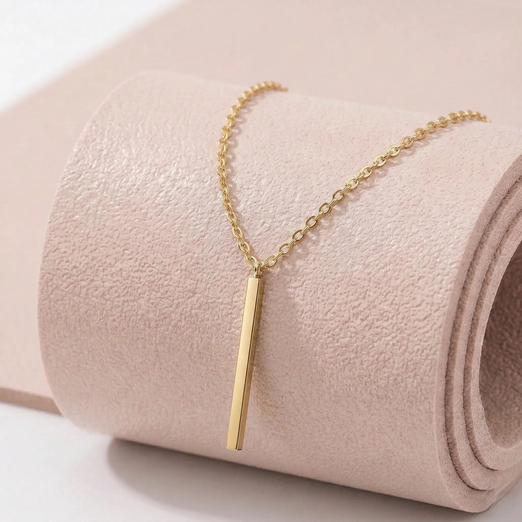 Gold stainless steel necklace with a vertical bar pendant on a light pink fitness mat.