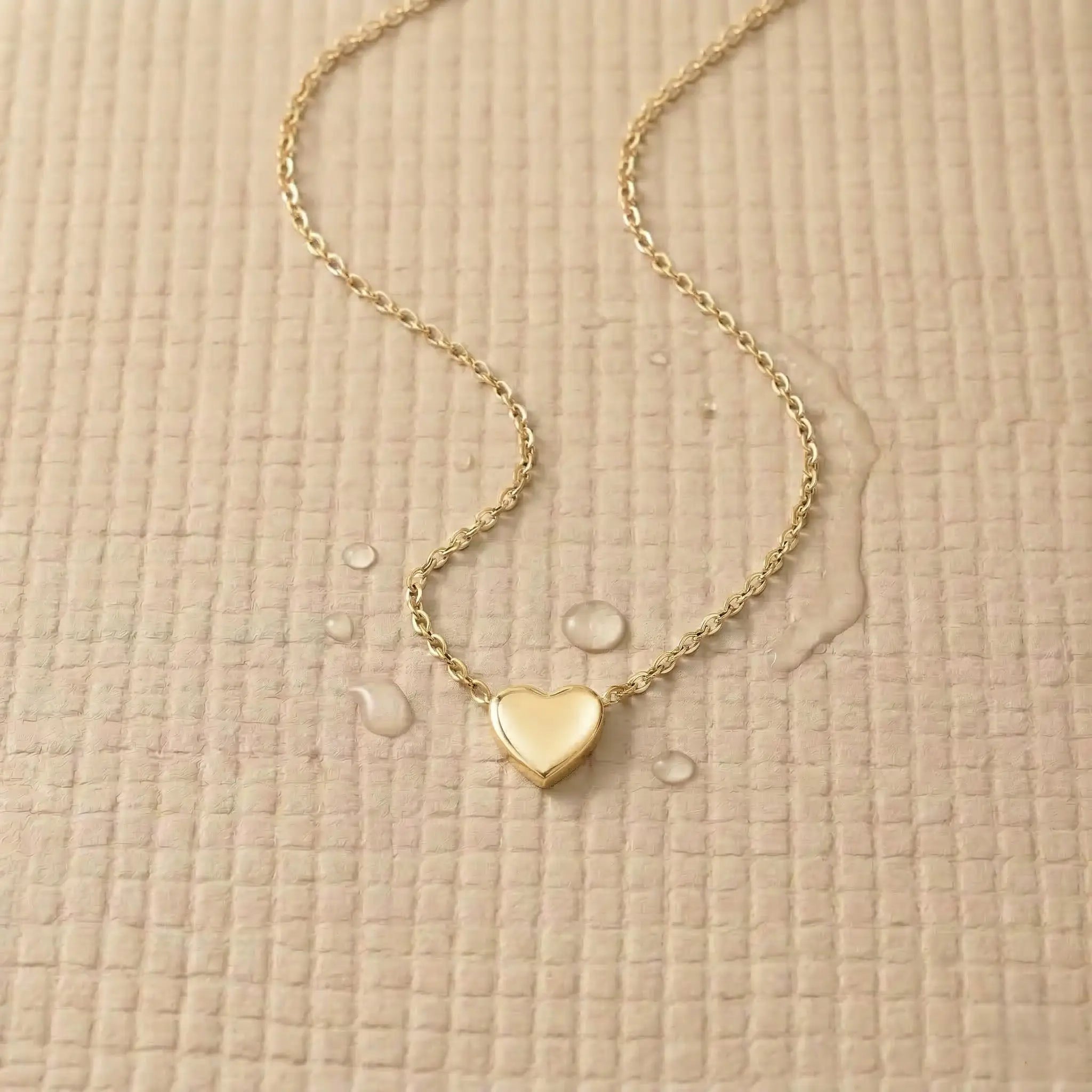Gold stainless steel heart pendant on a light pink fitness mat.