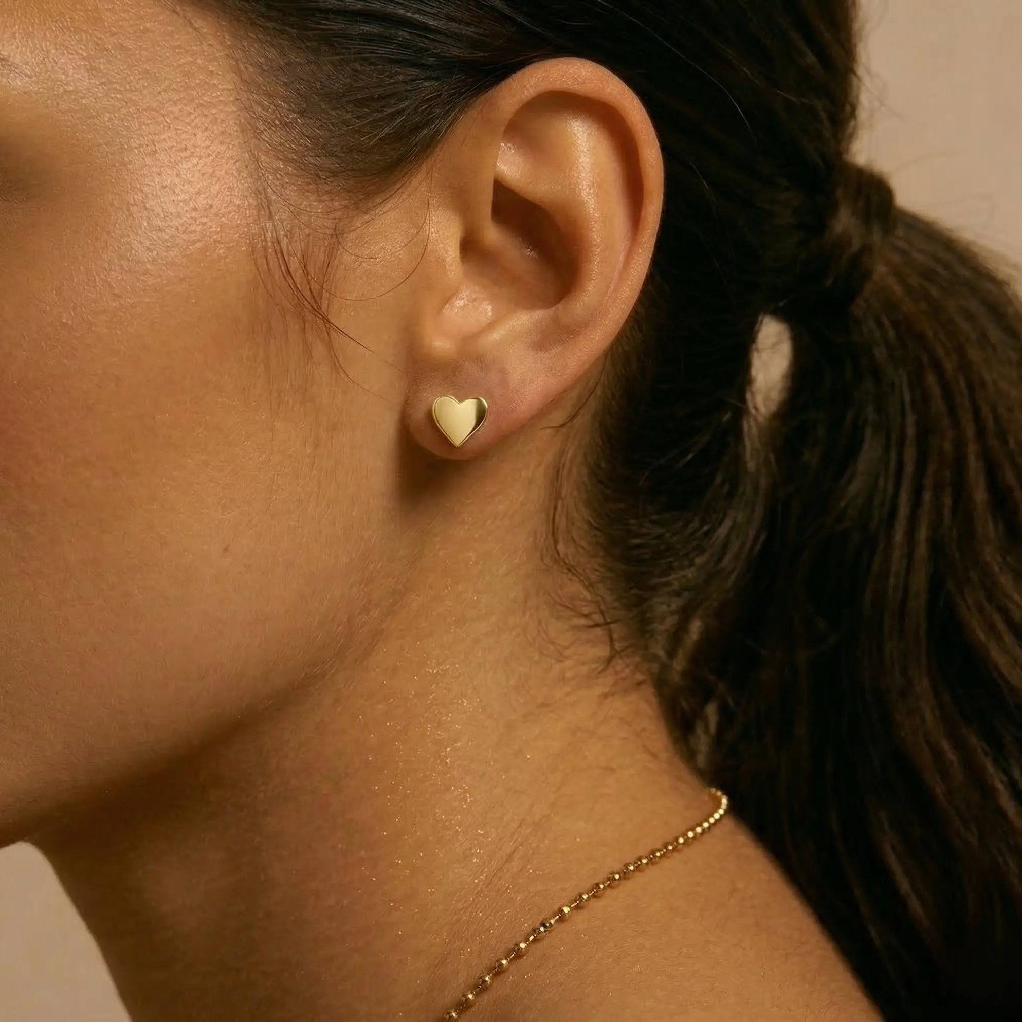 Close-up of a woman wearing a gold heart-shaped earring with a blurred background.