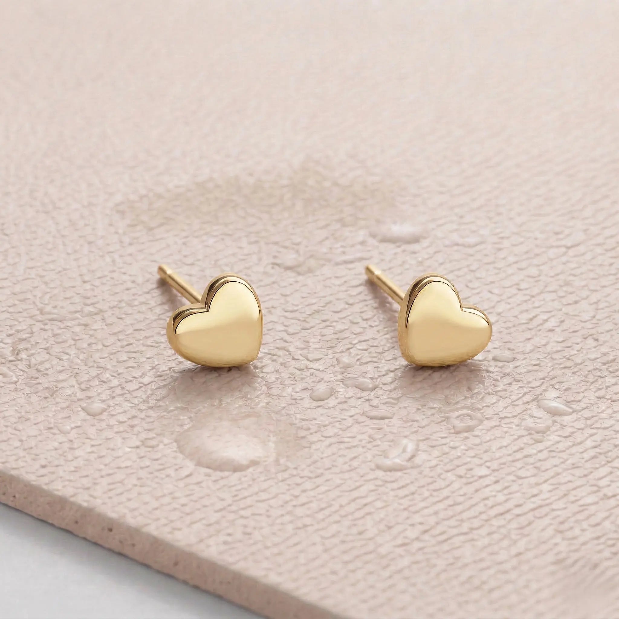 Waterproof heart gold stud earrings on a light pink fitness mat.