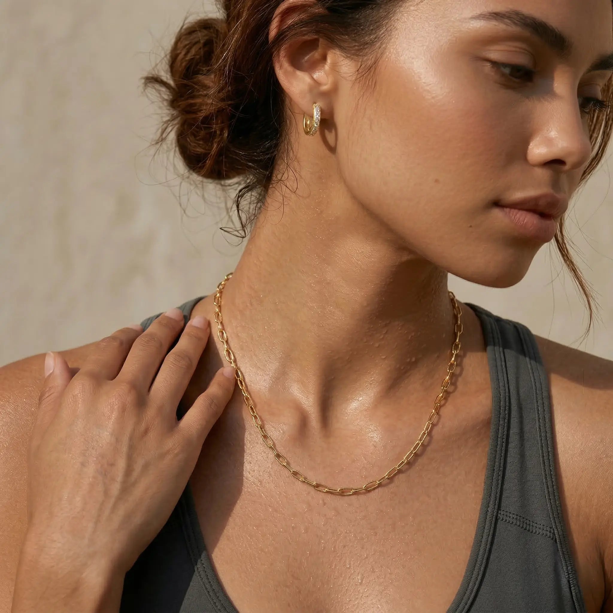 Woman wearing a gold-plated chain necklace with a neutral background.