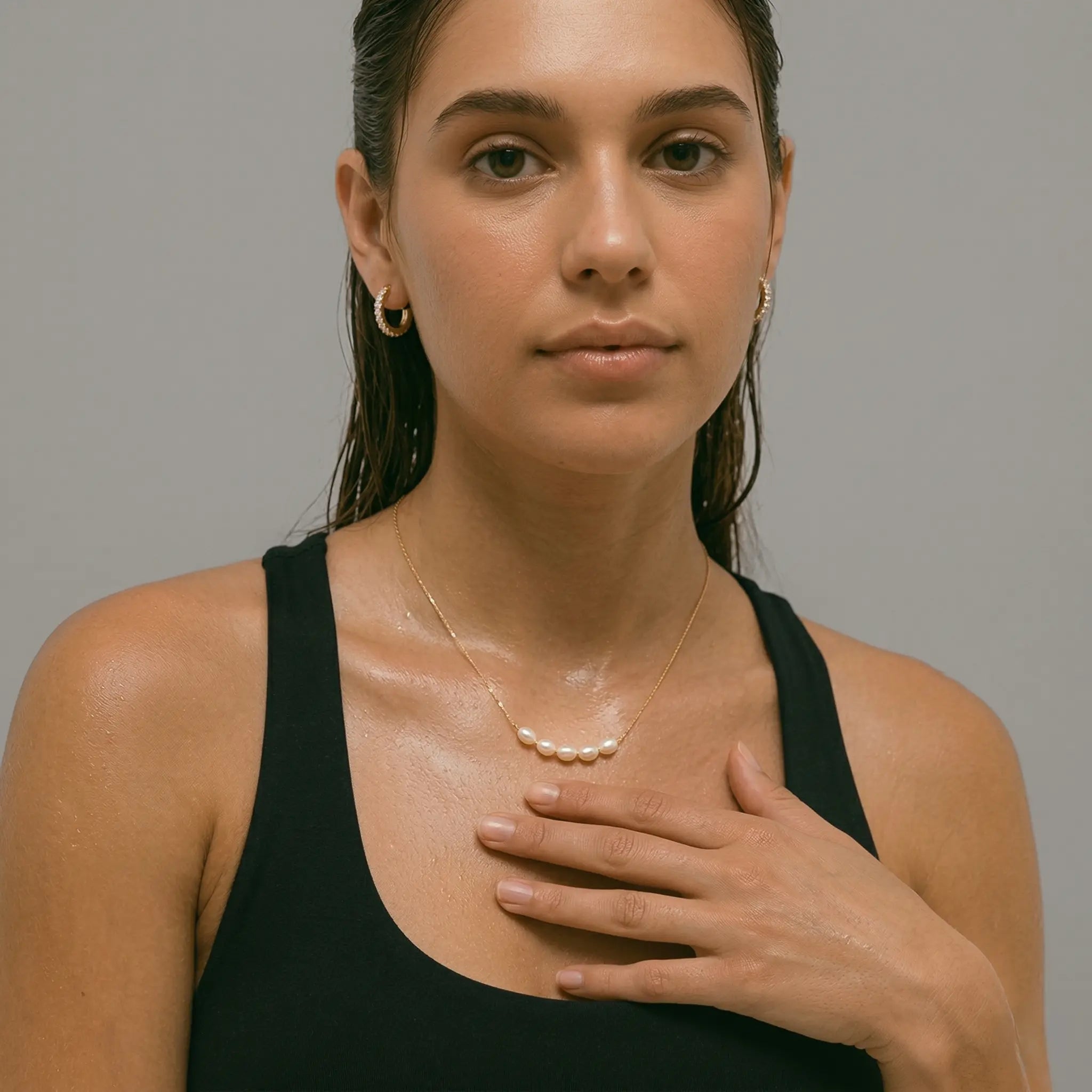 Woman wearing a black top and gold-plated necklace with pearls against a gray background.