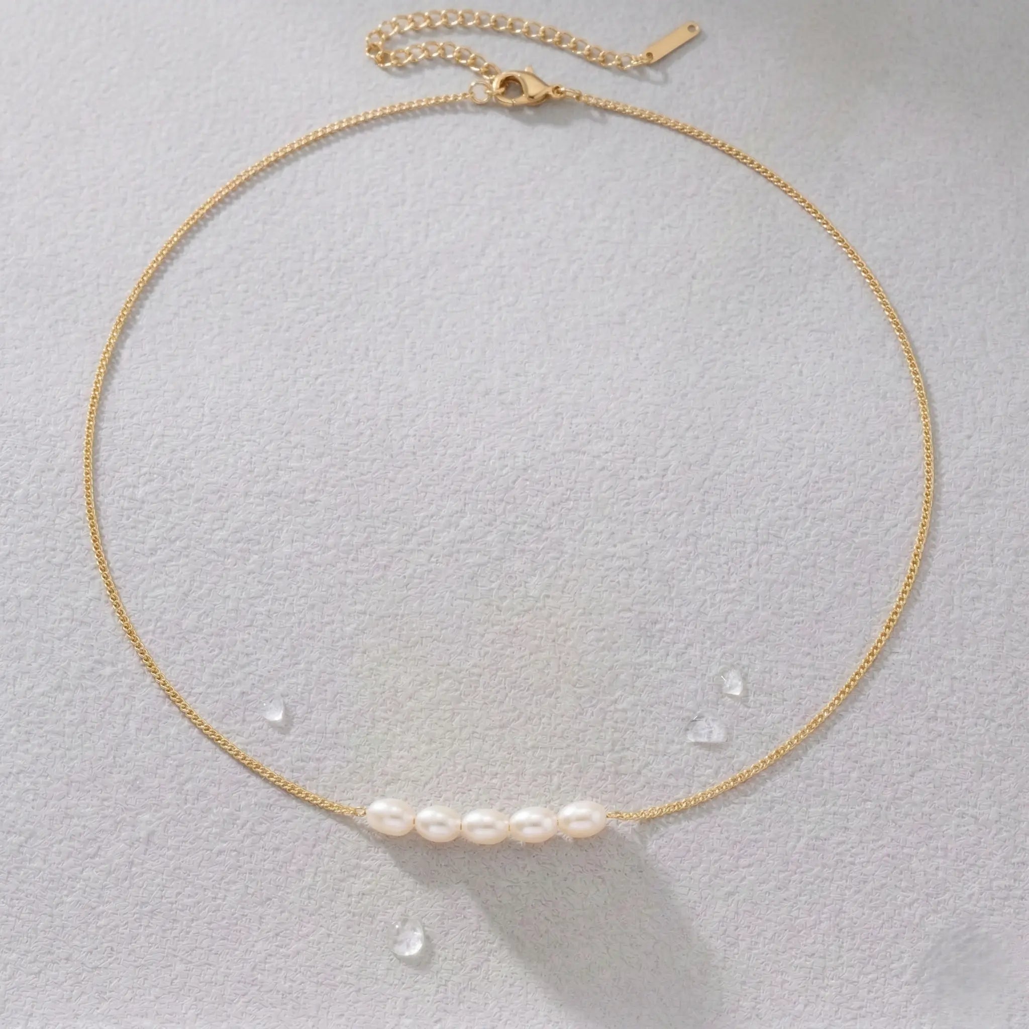 Gold-plated necklace with pearls on a light gray background.
