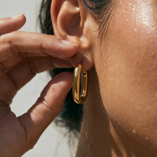 Gold rectangular hoop earring being worn and adjusted by a hand.