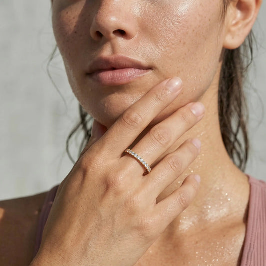 Close-up of a woman's hand with a diamond ring on her finger, touching her neck.