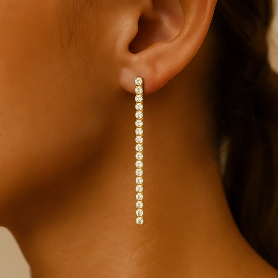 Close-up of an ear wearing a long  gold diamond earring.