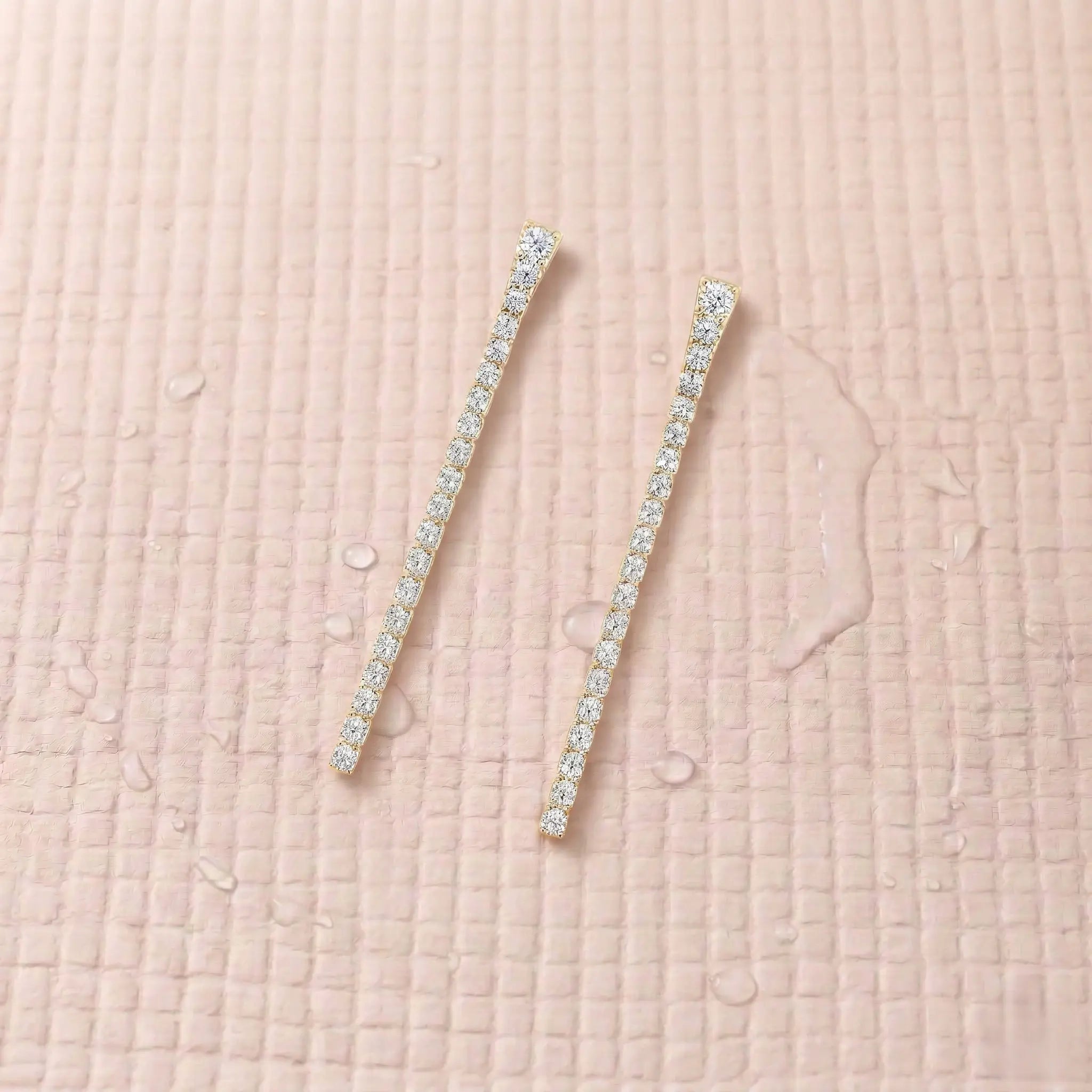 Pair of gold-plated diamond earrings on a light pink fitness mat.