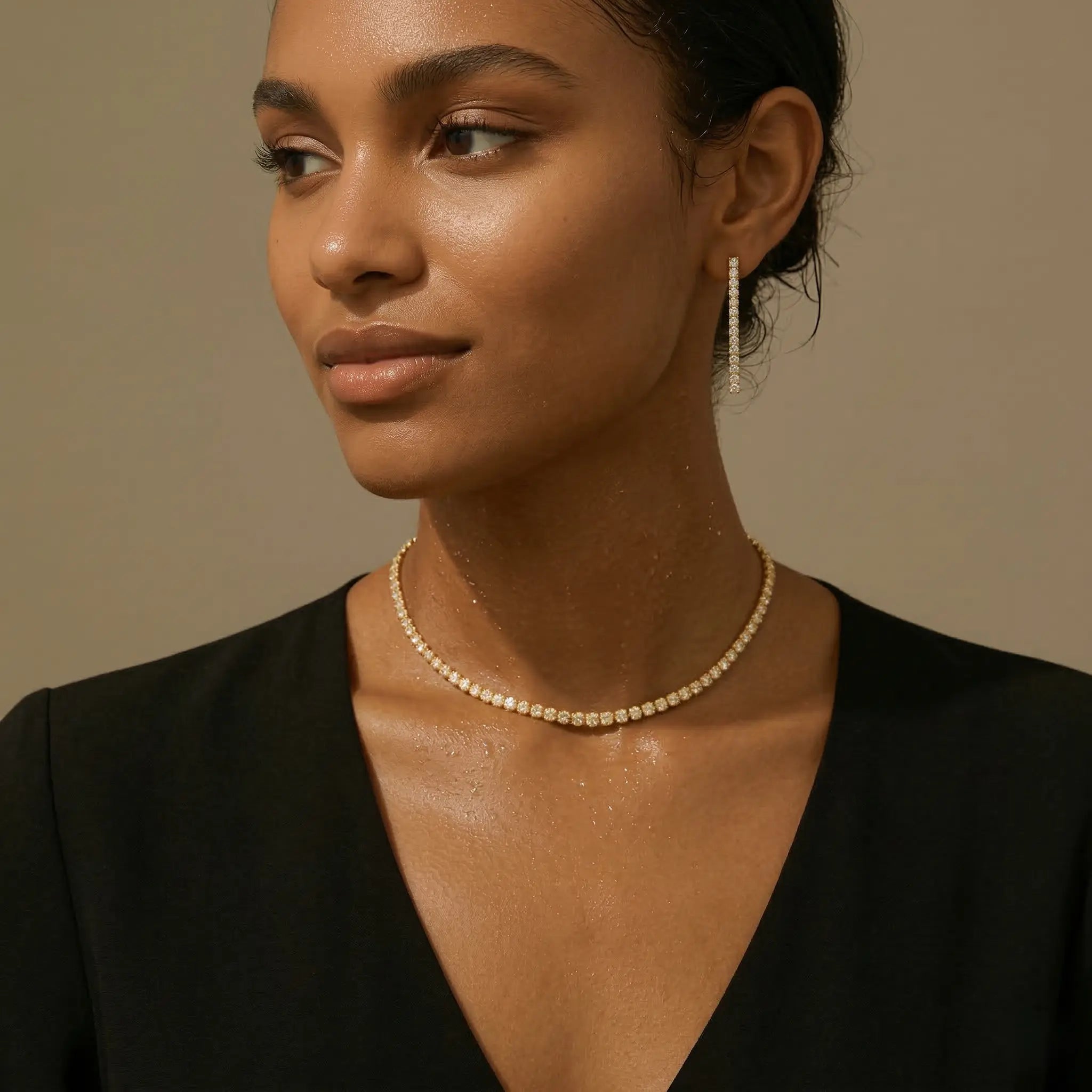 Woman wearing a gold zirconia necklace and matching drop earrings against a beige background.