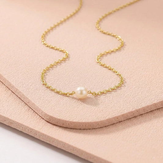 Gold sweatproof necklace with a single pearl on a light pink fitness mat.