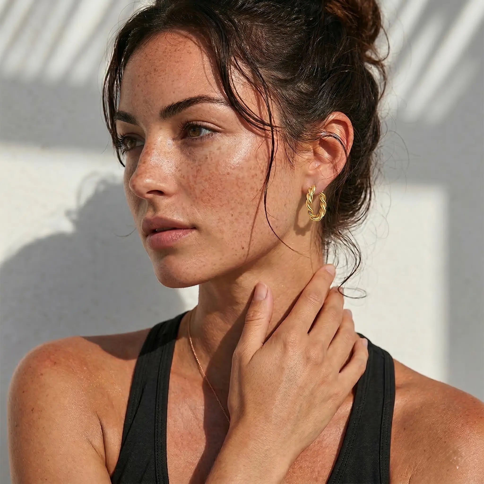 Woman wearing gold plated hoop earring against a white background.