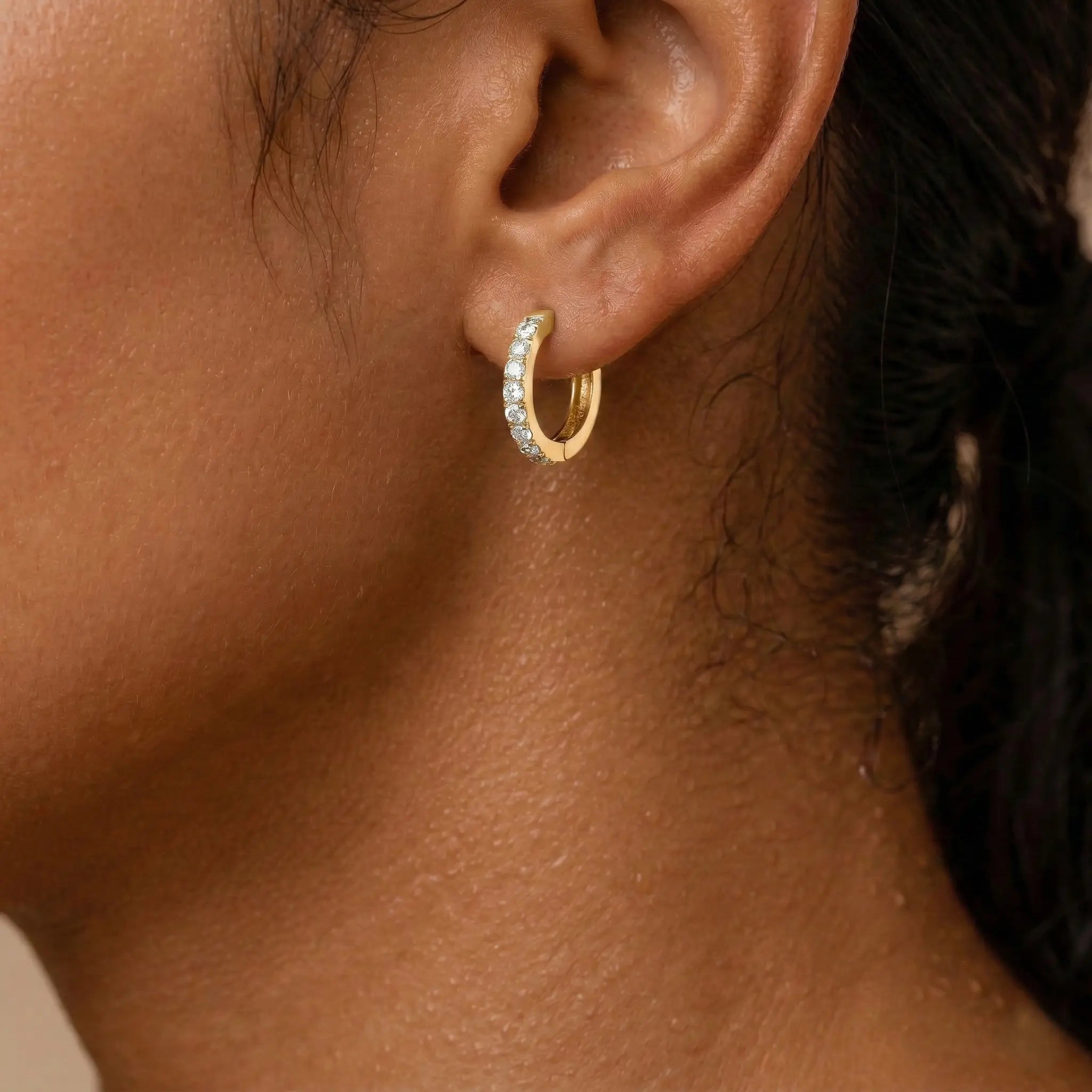 Close-up of an ear wearing a gold hoop earring with clear stones.
