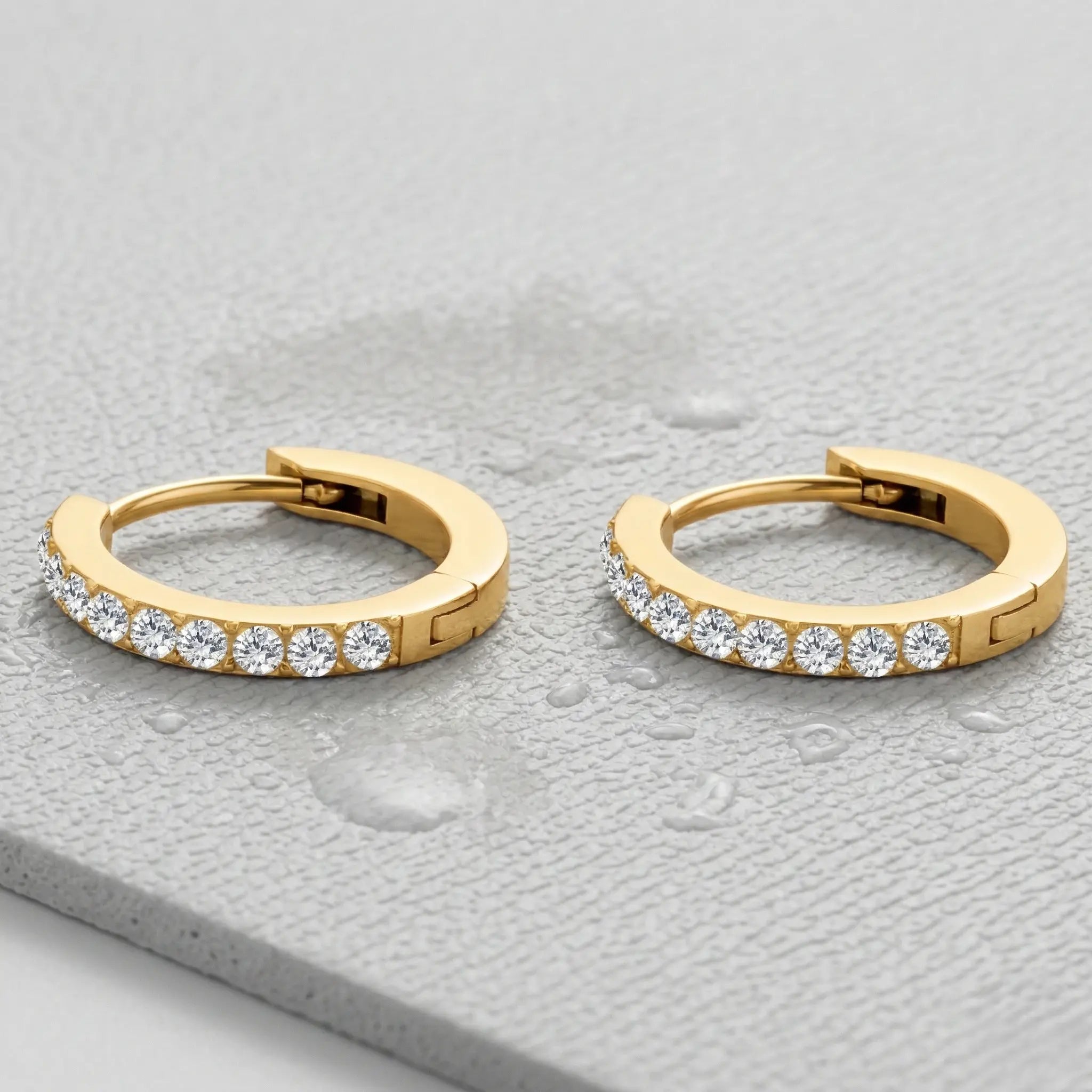 Gold-plated hoop earrings with embedded diamonds on a light gray fitness mat.
