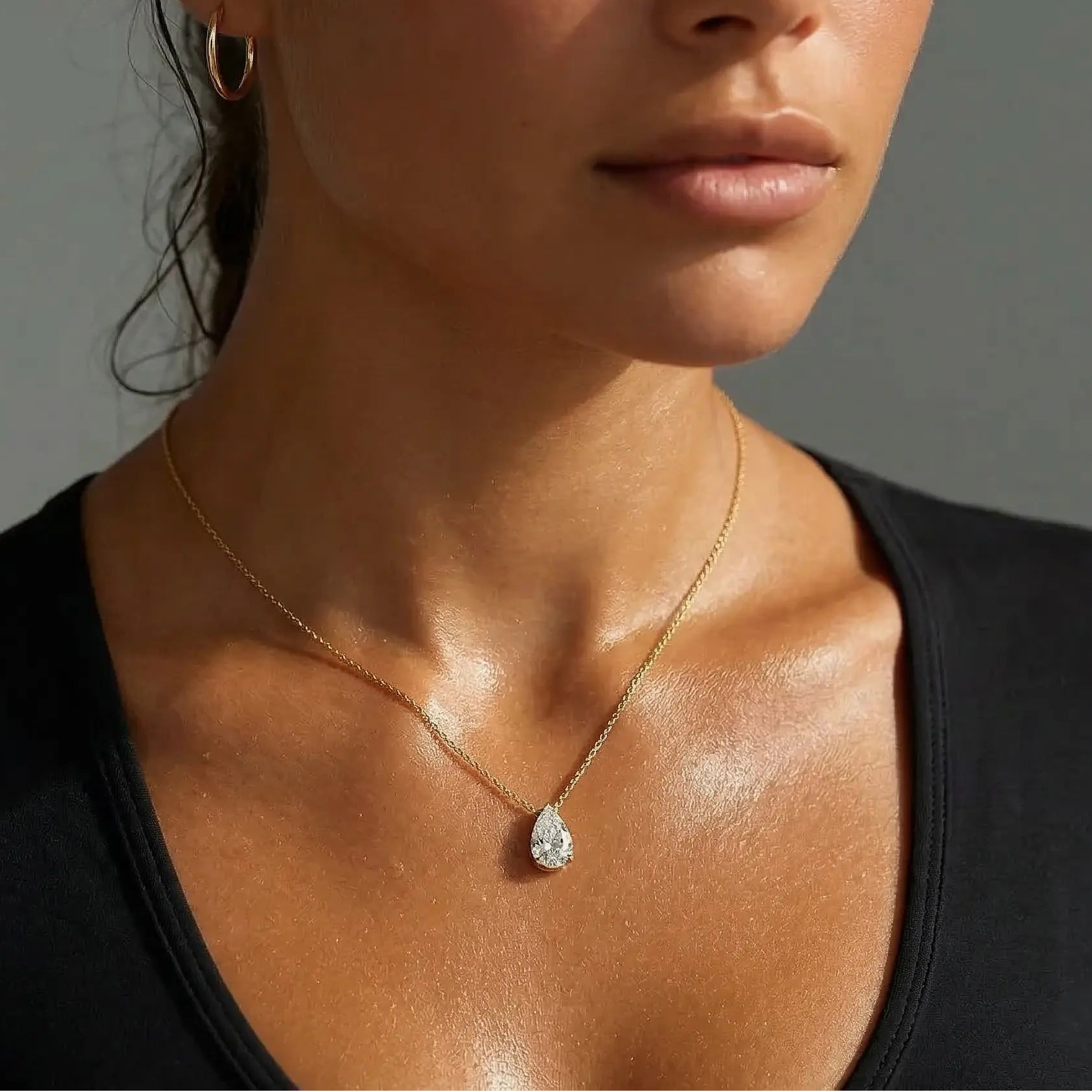 Woman wearing a gold necklace with a diamond pendant against a neutral background.