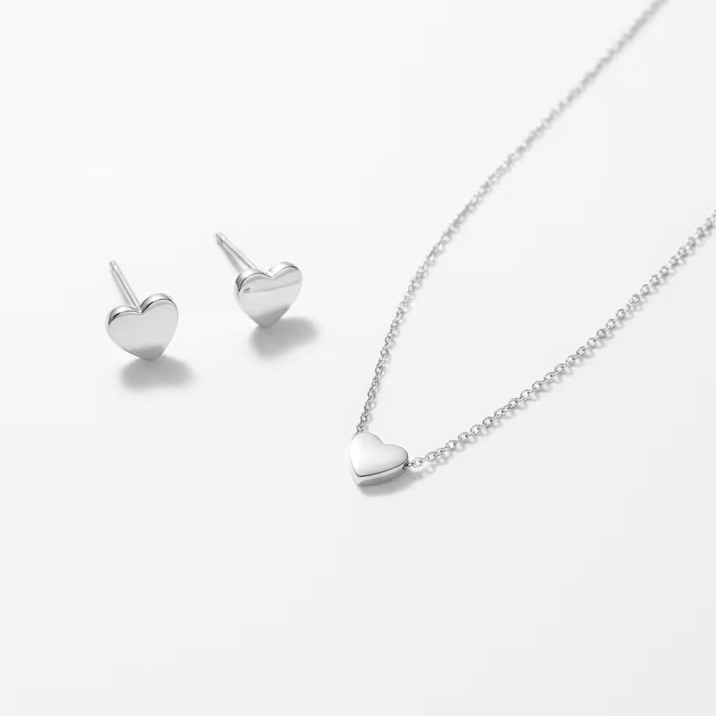Silver heart-shaped necklace and matching stud earrings on a white background.