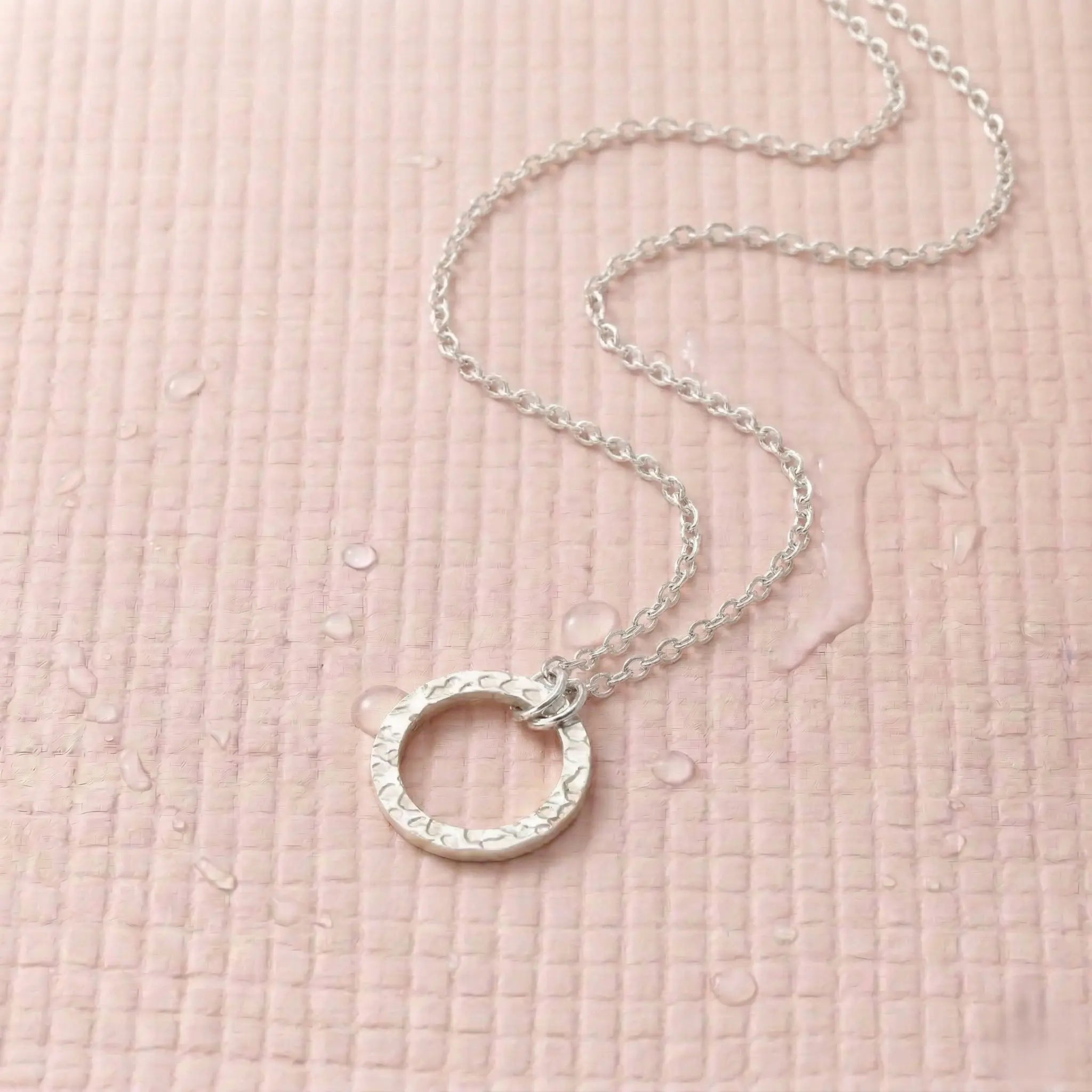  Silver-plated necklace with a circle pendant on a light pink fitness mat.