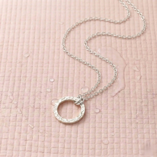 Silver-plated necklace with a circle pendant on a light pink fitness mat.