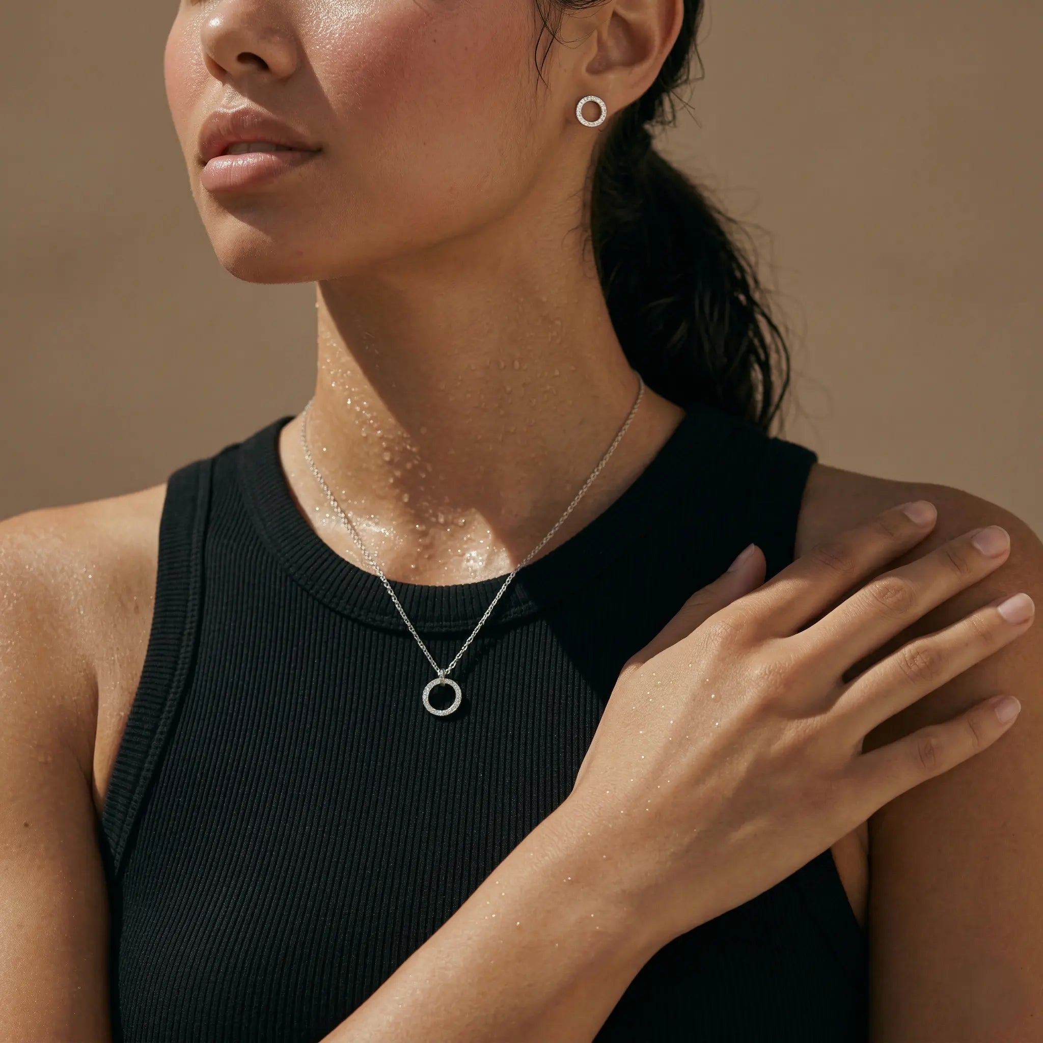 Woman wearing a silver circle necklace and matching stud earrings against a warm brown background.