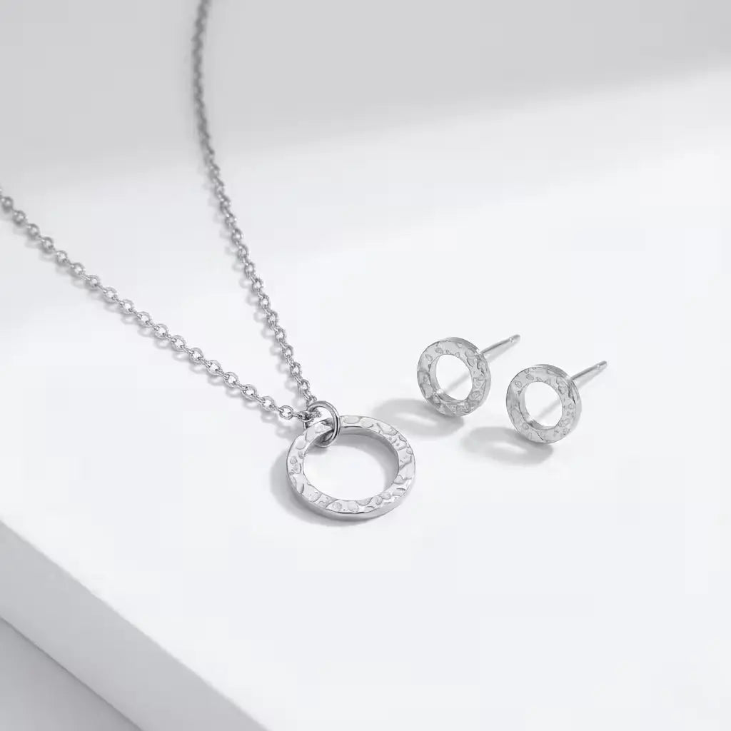 Silver circle necklace and matching studs on a light gray background.