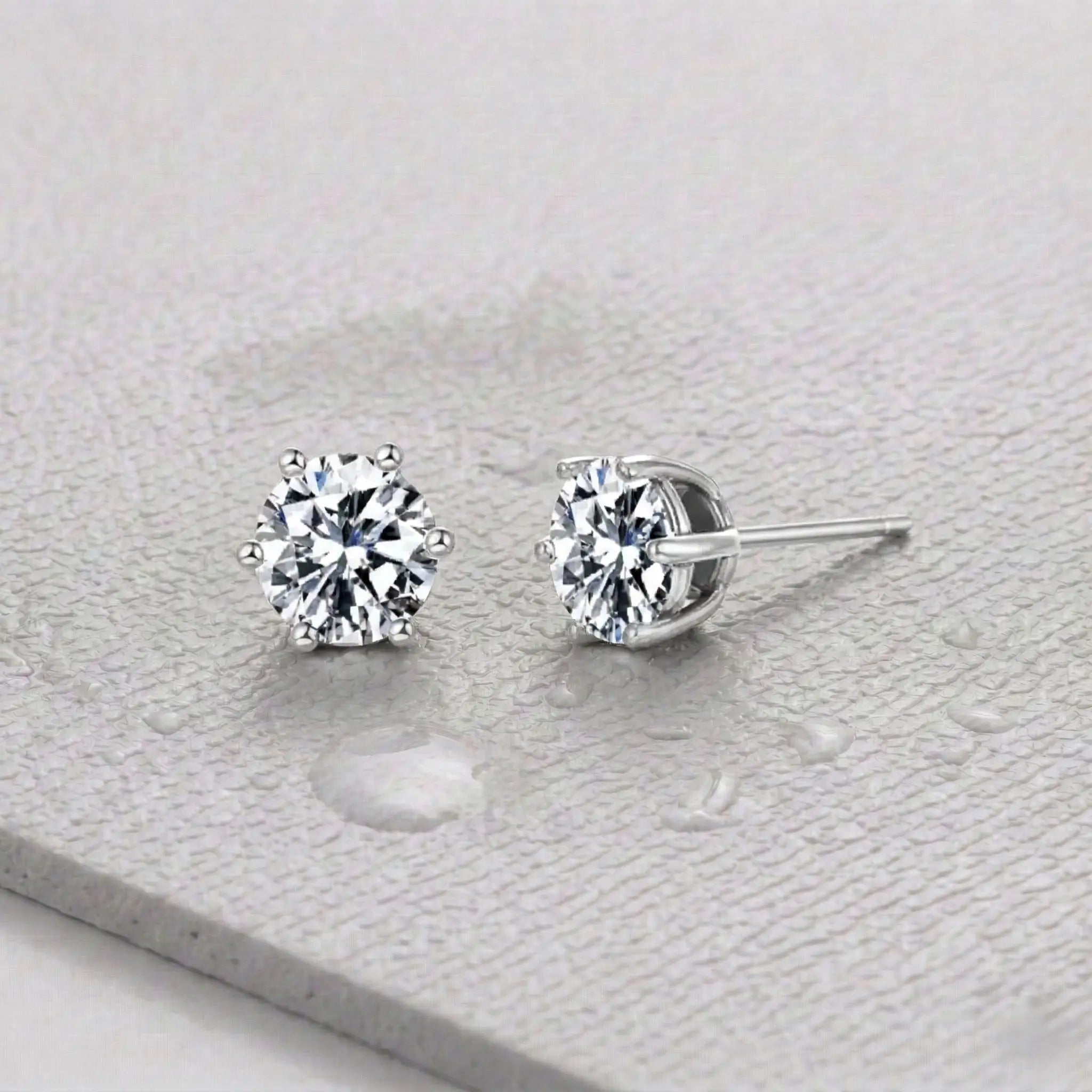 Pair of silver zirconia stud earrings on a light gray fitness mat.