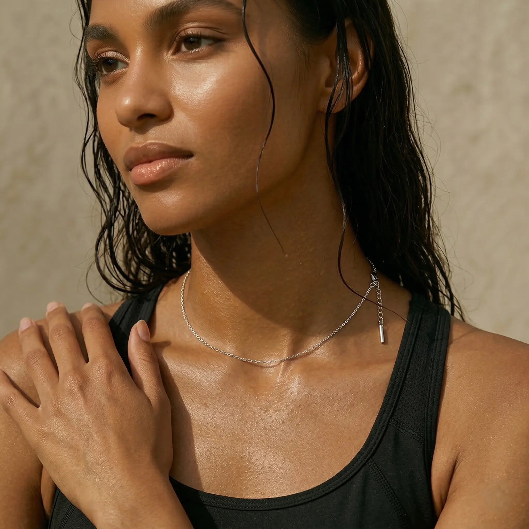 Woman with wet hair wearing a black top and silver necklace against a neutral background.