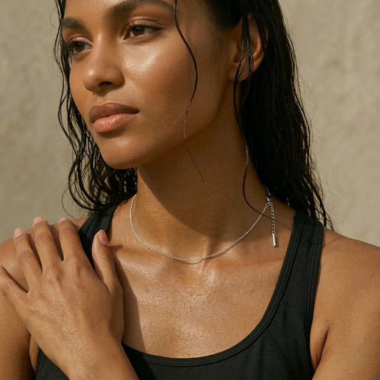 Woman with wet hair wearing a black top and silver necklace against a neutral background.