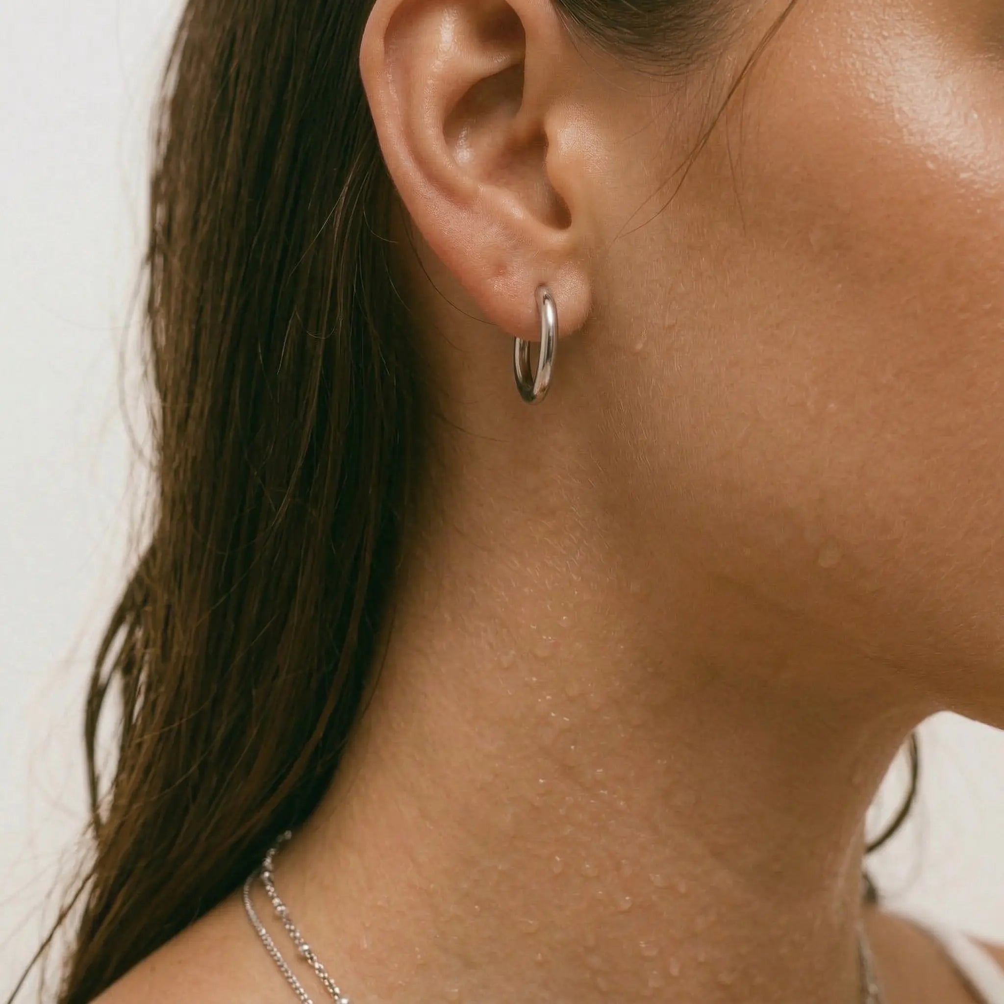 Close-up of an ear wearing a silver hoop earring with a neutral background.