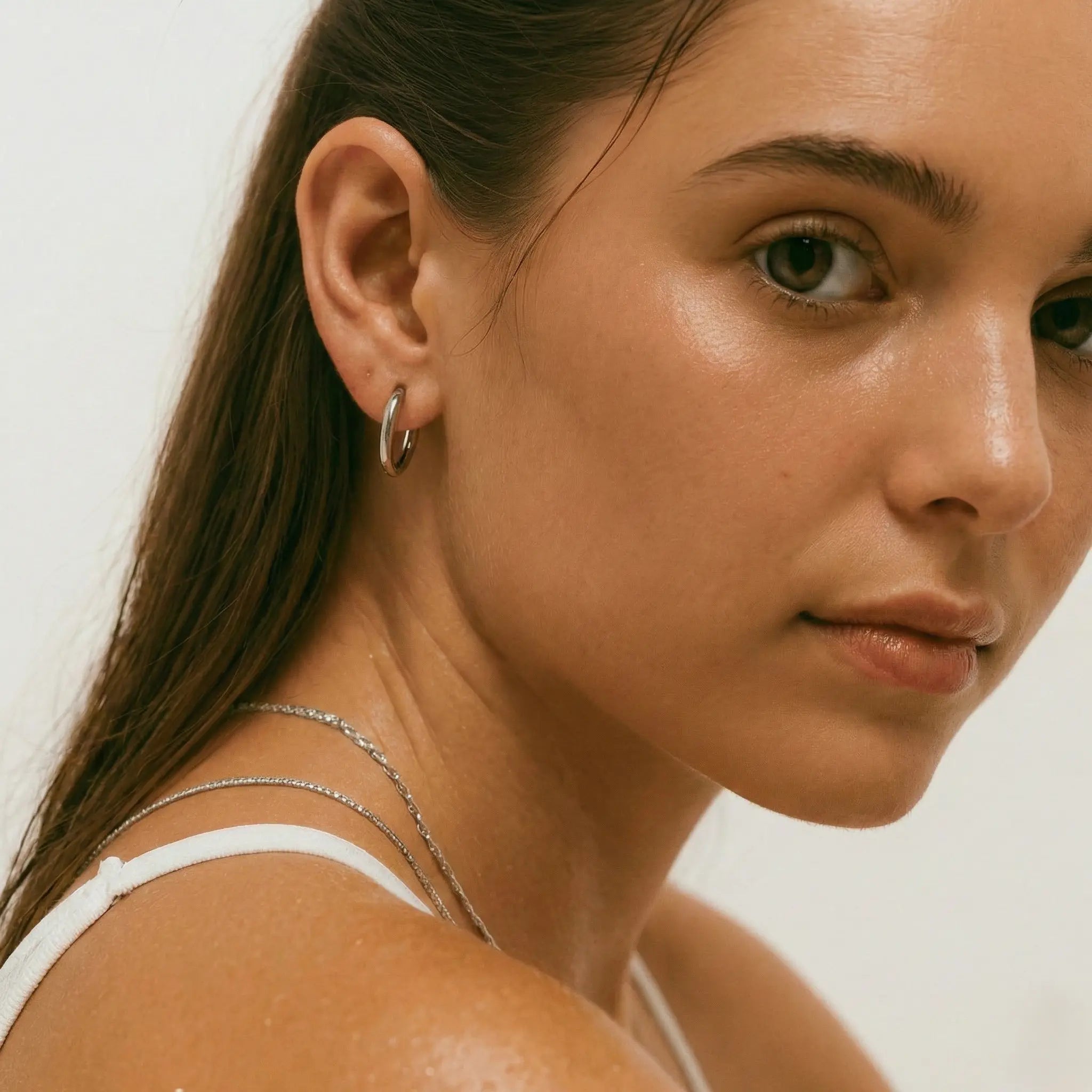 Close-up of a woman wearing a silver-plated hoop earring against a neutral background.