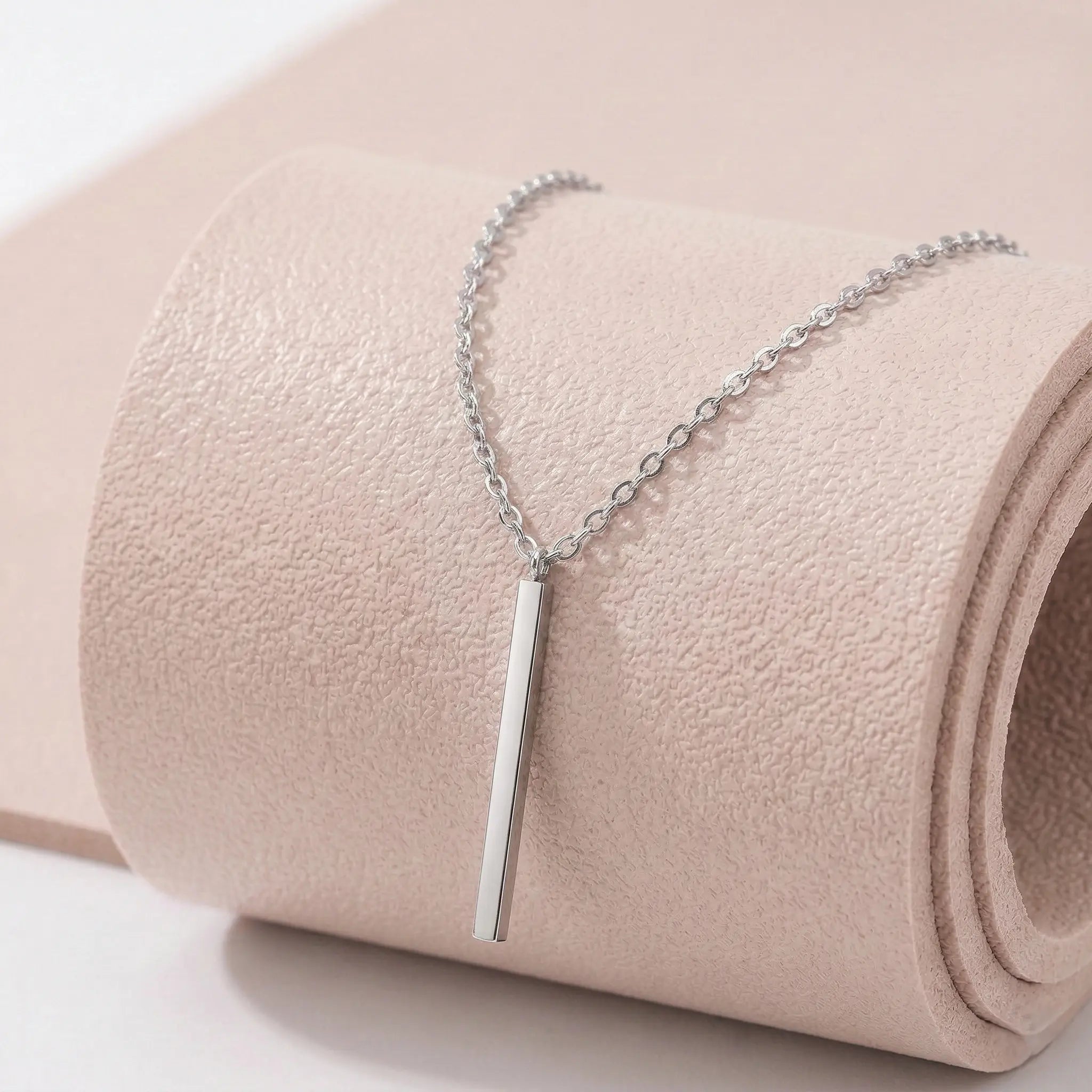 Silver stainless steel necklace with a vertical bar pendant on a light pink fitness mat.