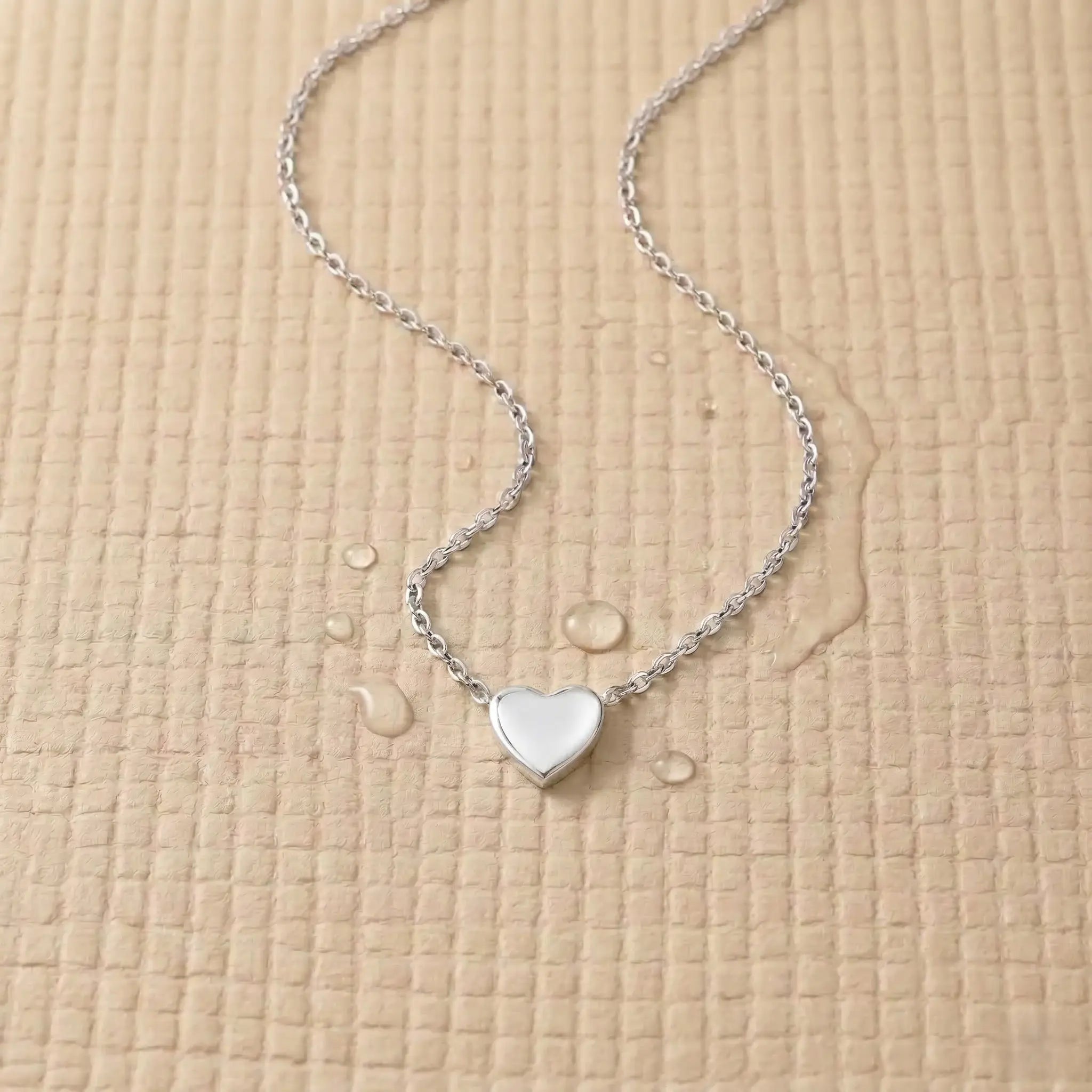 Silver stainless steel heart pendant on a light pink fitness mat.