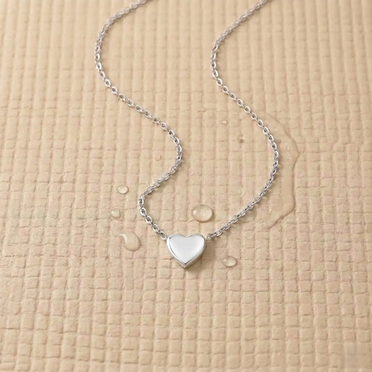 Silver stainless steel heart pendant on a light pink fitness mat.