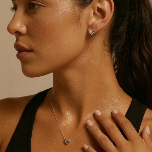 Close-up of a woman wearing a silver heart-shaped necklace and matching stud earrings.