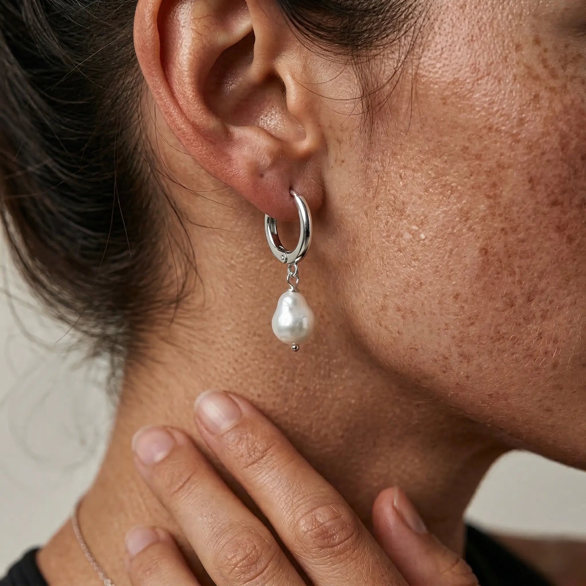 Close-up of an ear wearing a silver hoop earring with a pearl pendant.