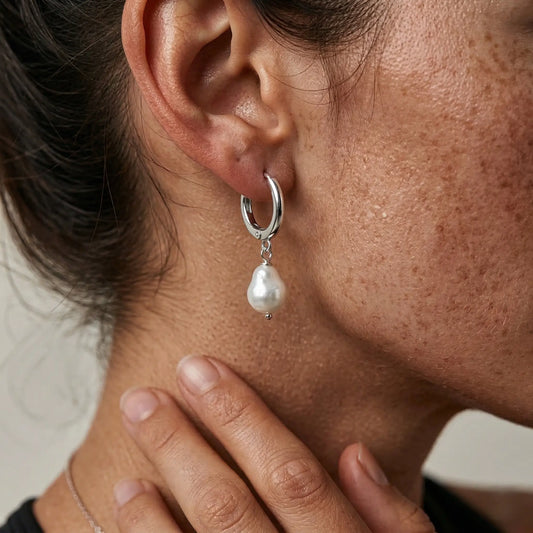 Close-up of an ear wearing a silver hoop earring with a pearl pendant.