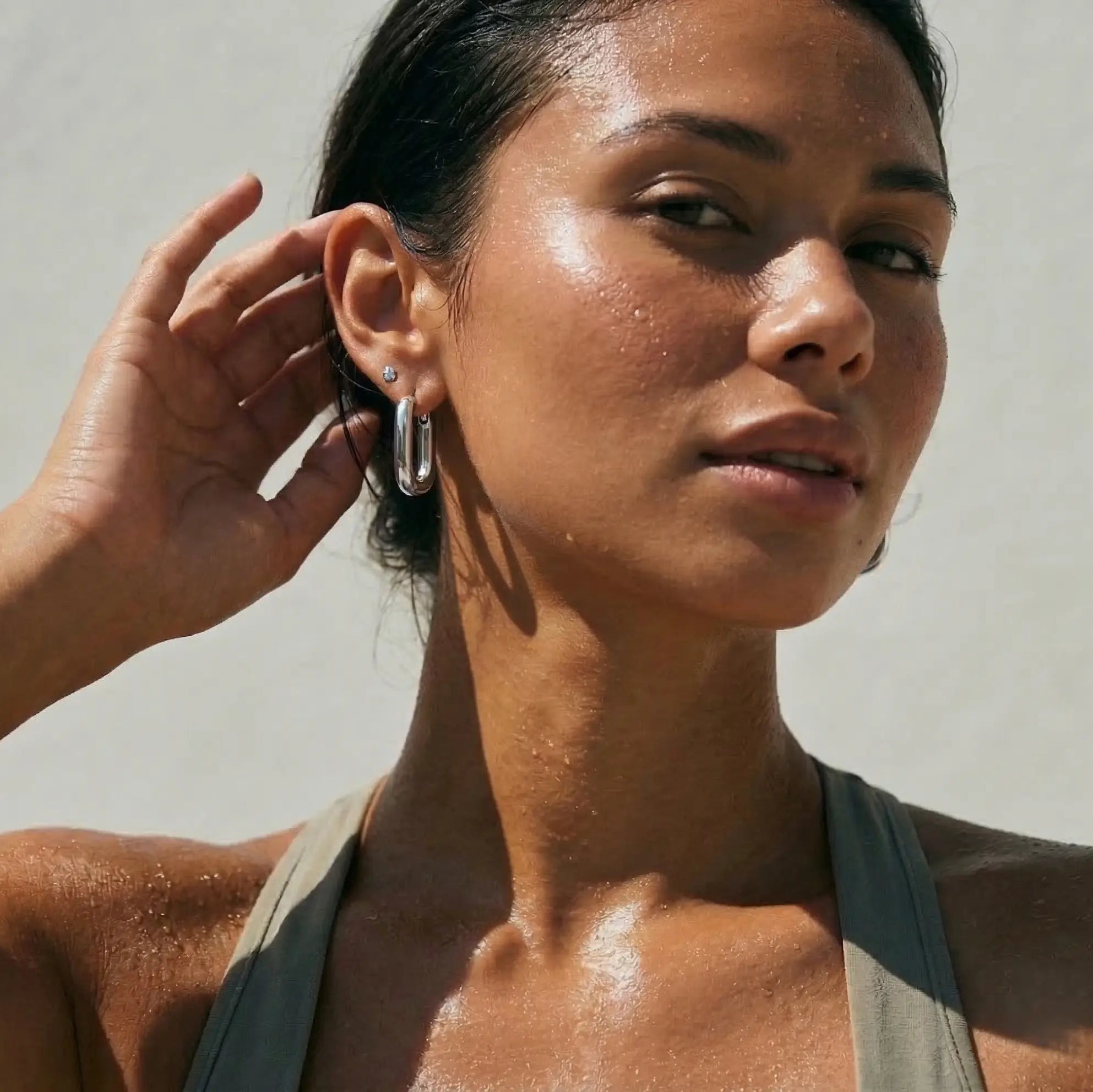 Athletic woman with rectangular silver hoop earrings against a neutral background.