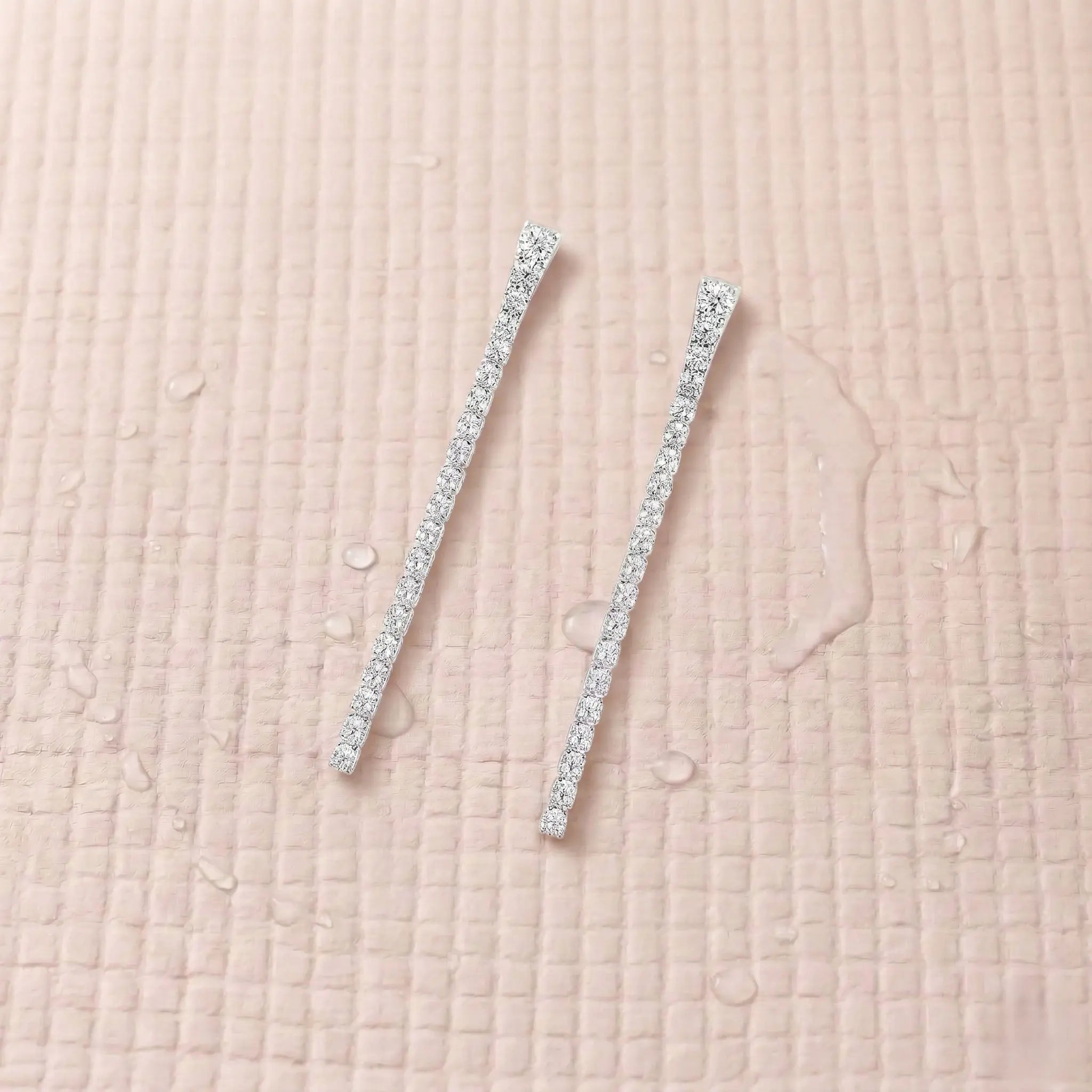 Pair of silver-plated diamond earrings on a light pink fitness mat.