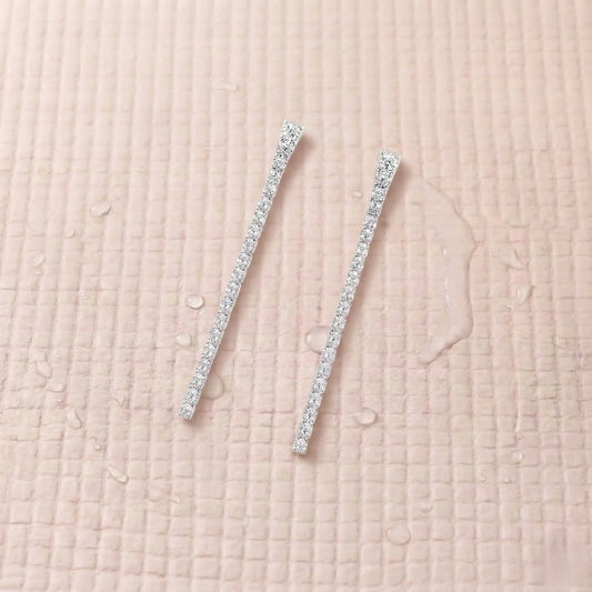 Pair of silver-plated diamond earrings on a light pink fitness mat.