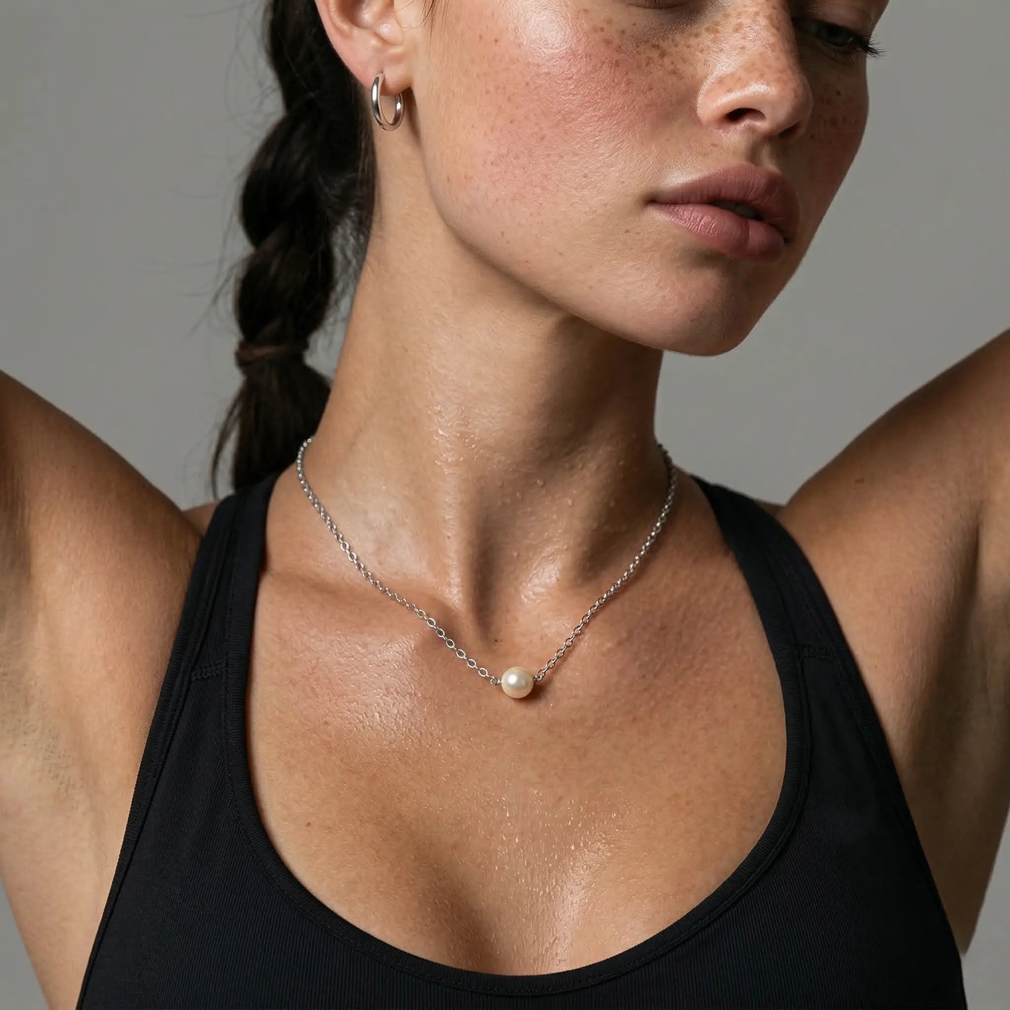 Close-up of a woman wearing a black top and silver pearl necklace against a neutral background.