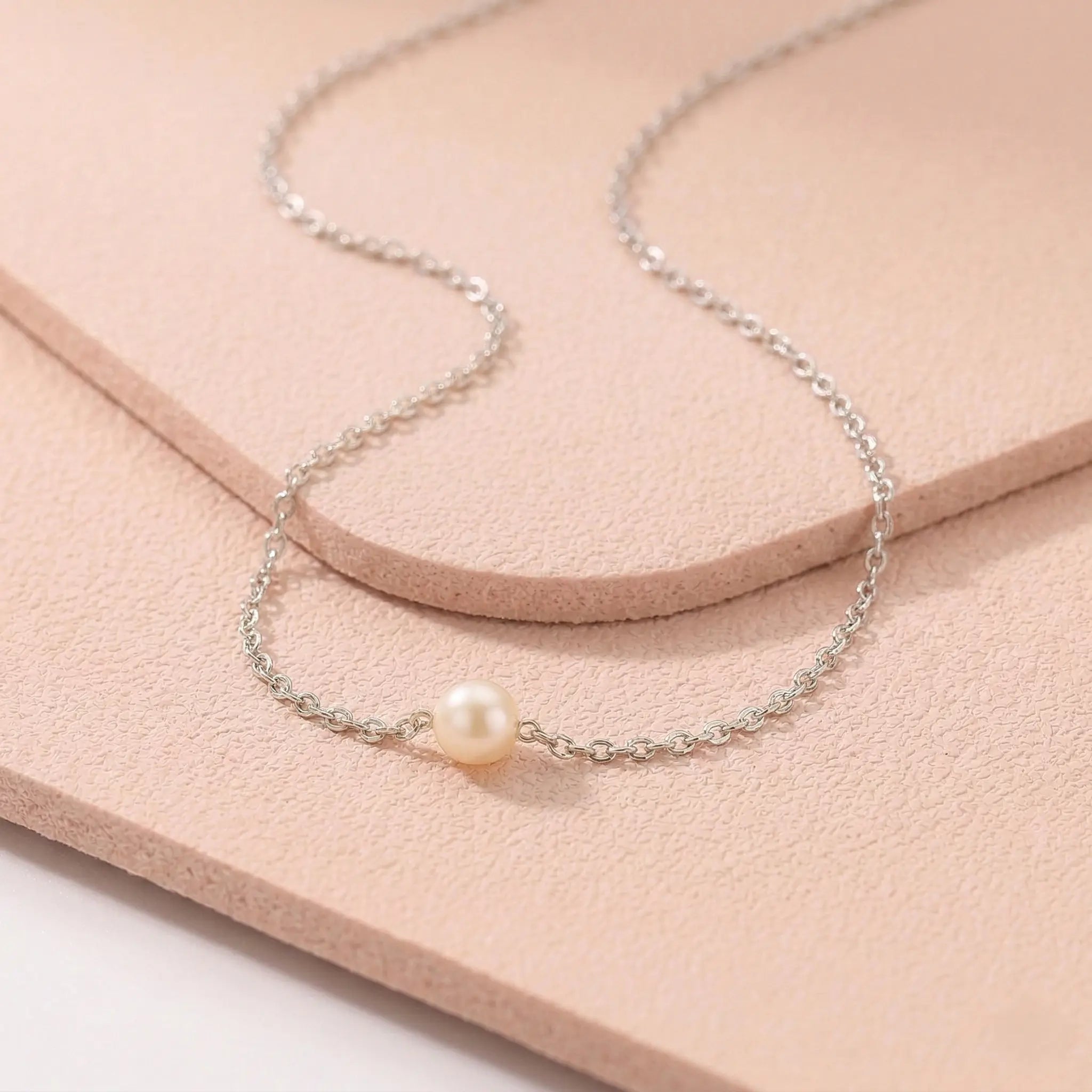 Silver sweatproof necklace with a single pearl on a light pink fitness mat.